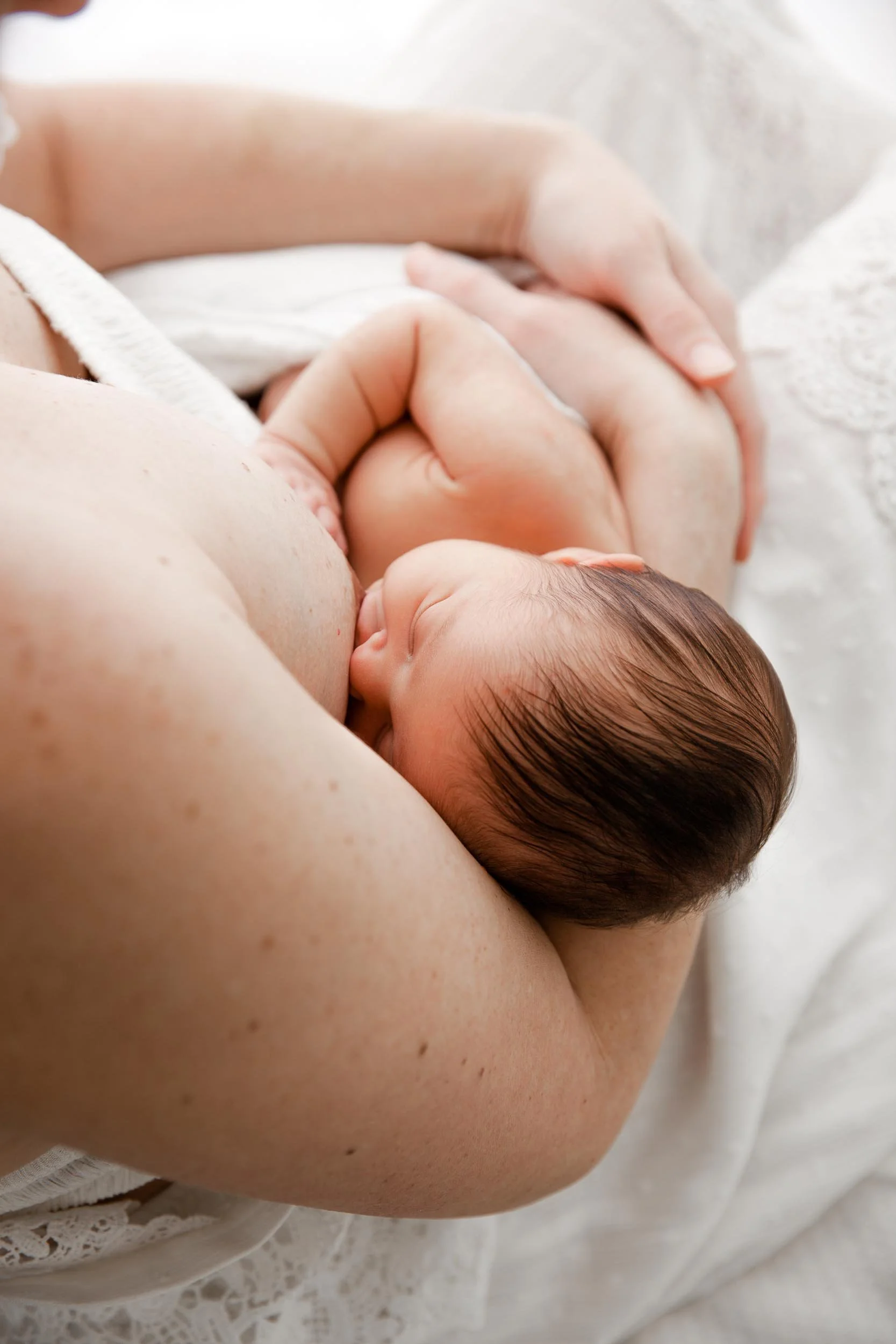 Newborn baby breastfeeding, held by a woman in a white lace garment.
