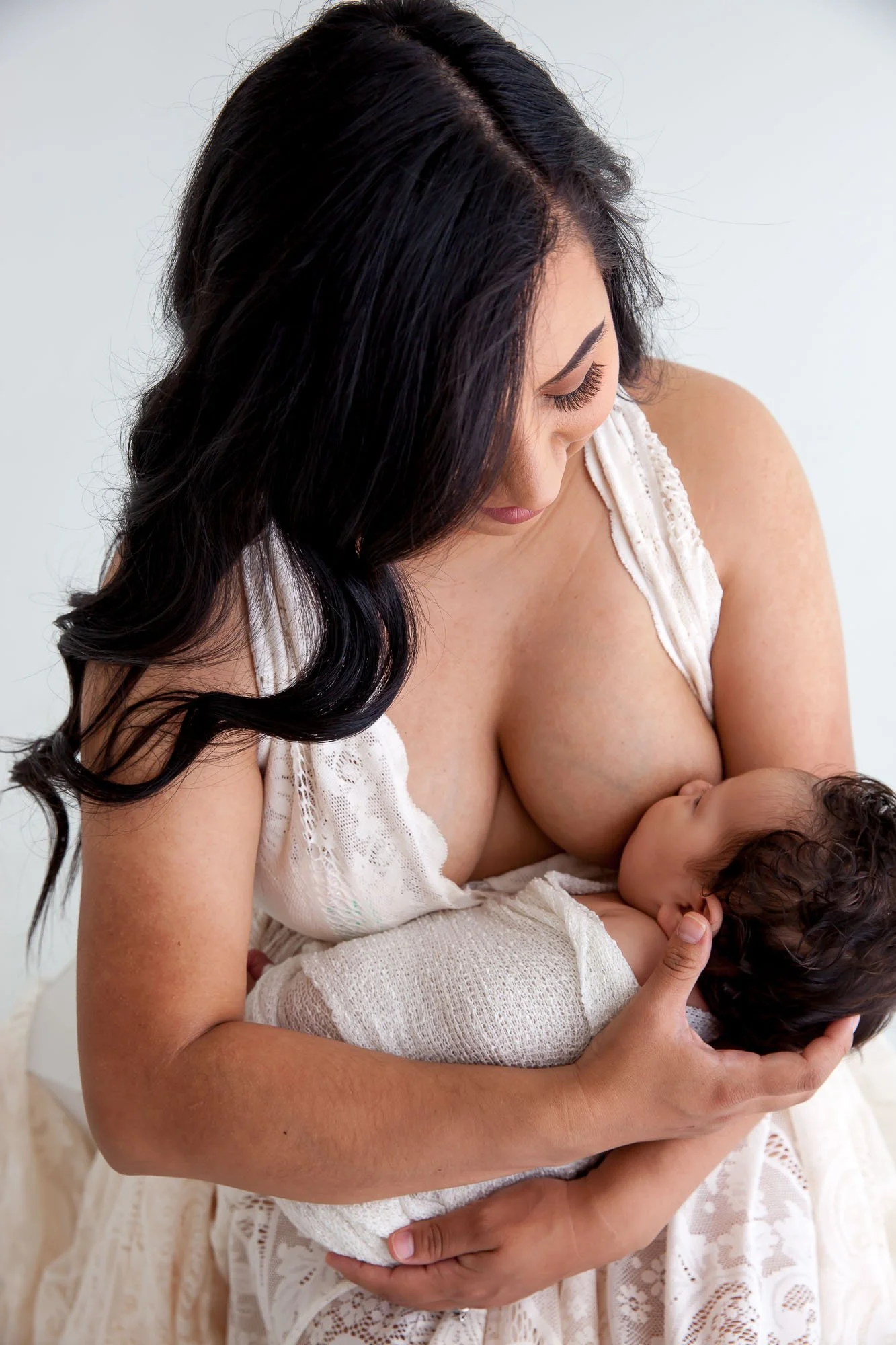A mother breastfeeding her baby in a tender moment, wearing a white lace dress.