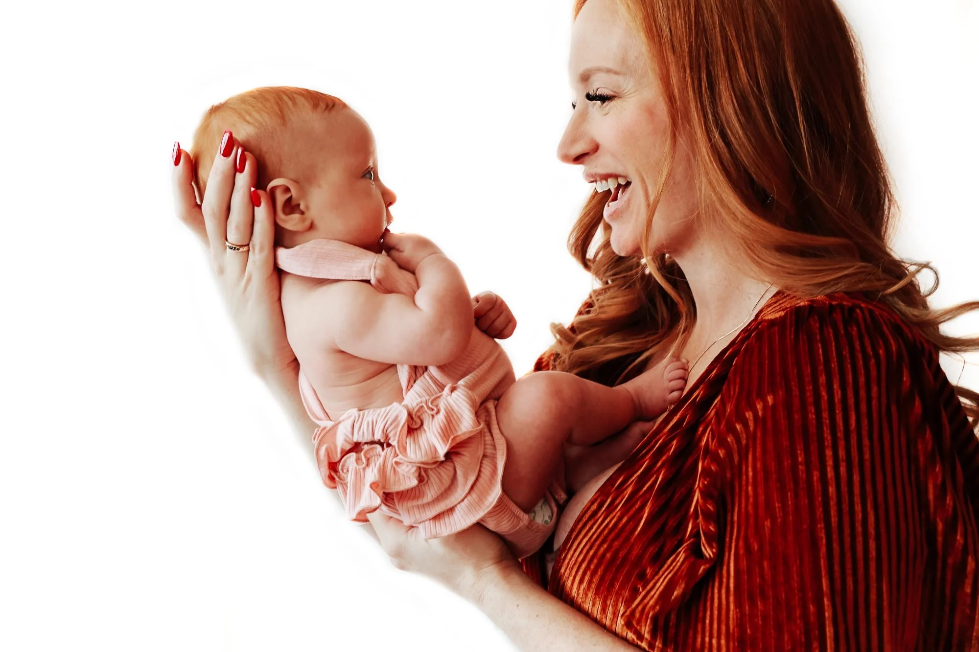 Woman holding and smiling at a baby, both with red hair, against a white background.