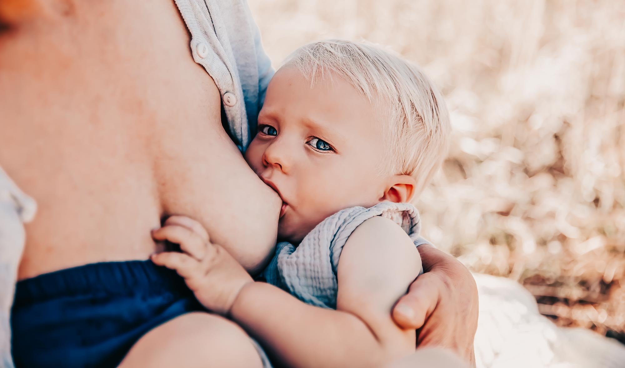 A baby breastfeeding outdoors with a parent's arm around them.
