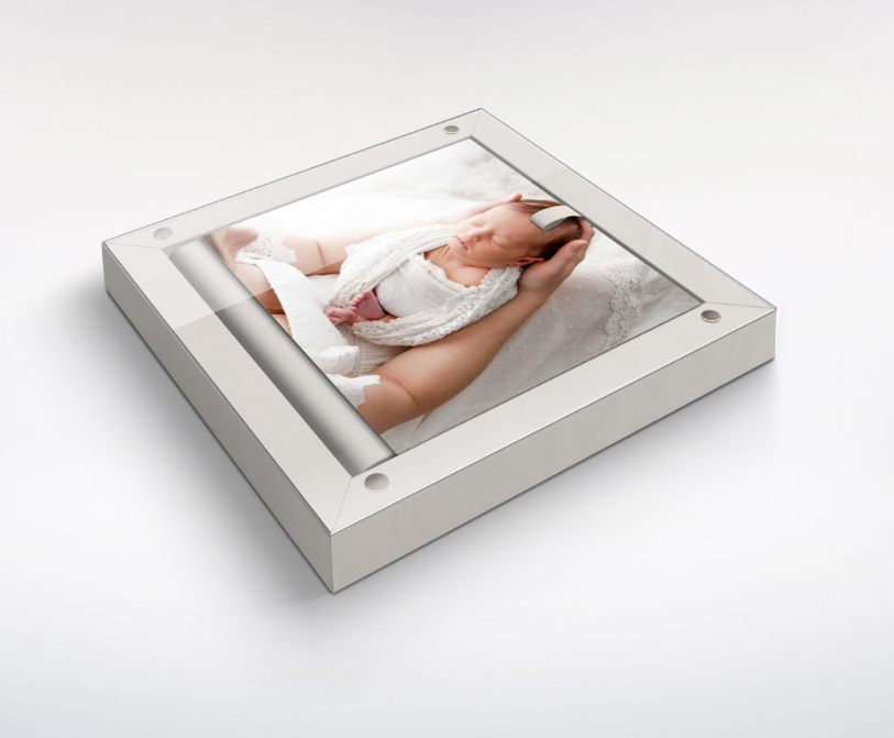 Framed photo of a sleeping baby wrapped in a white blanket, held by a person's arm.