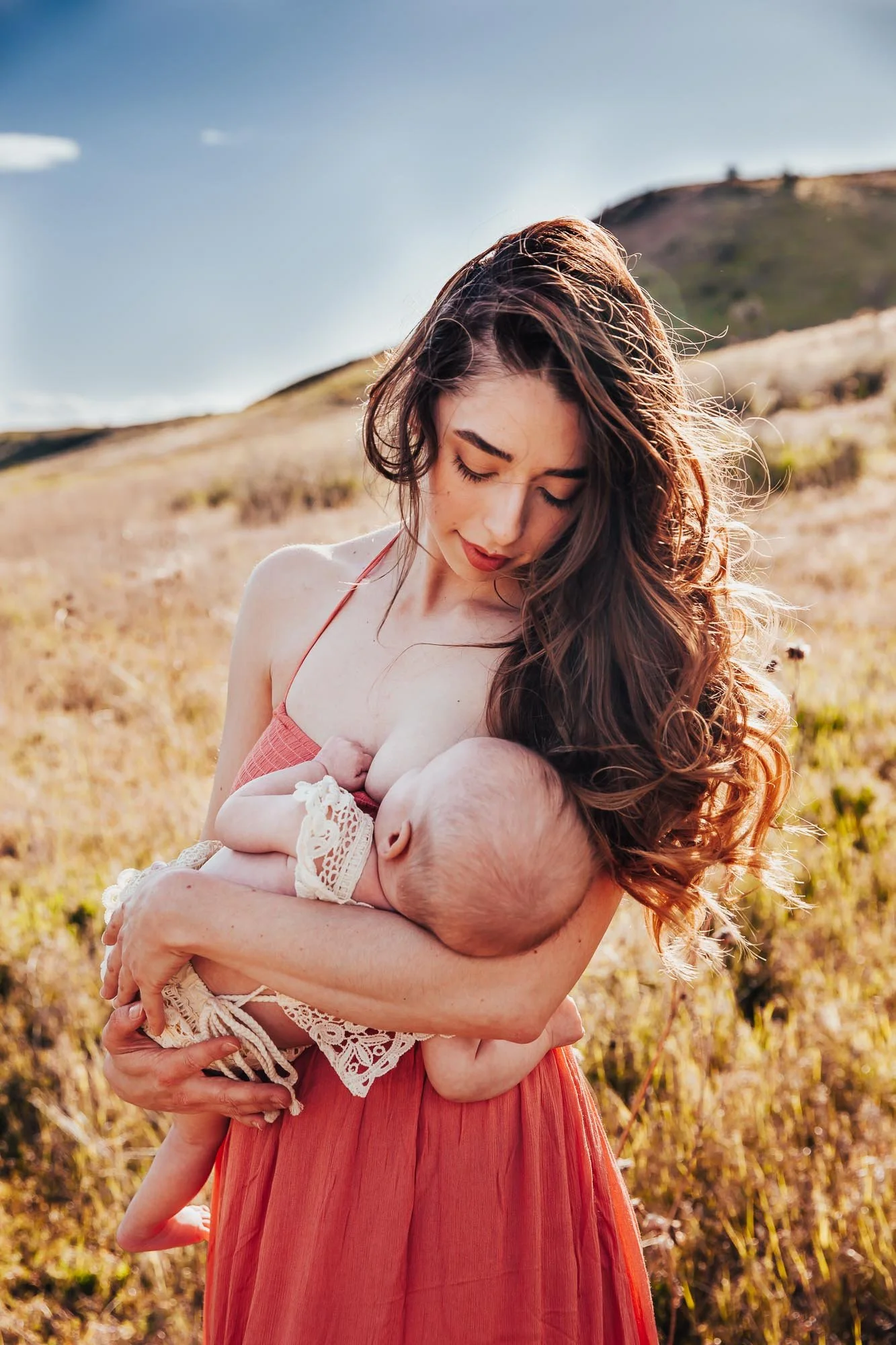 Photo of a breastfeeding mother holding her baby outside in a meadow