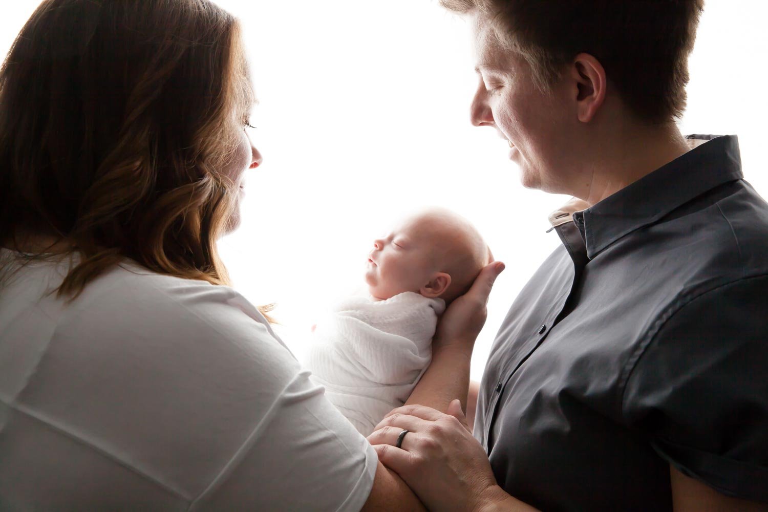 Backlit photo of two new parents with their newborn baby