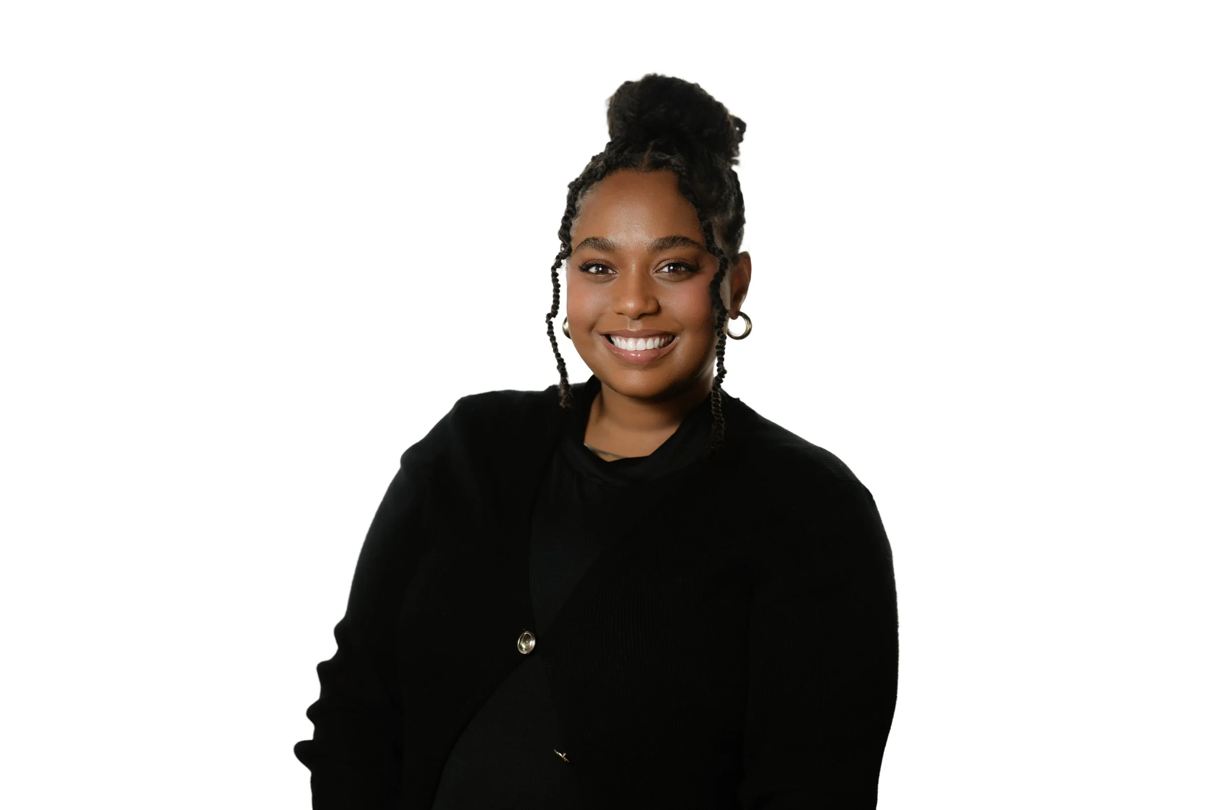 A woman smiling, wearing a black blazer, earrings, and a bun hairstyle, against a plain white background.