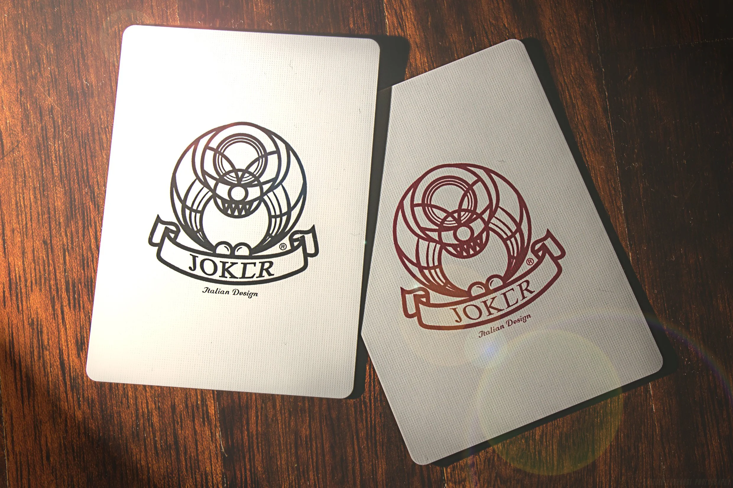 Two decks of Joker playing cards with a black and red logo of a joker's face on a wooden surface.