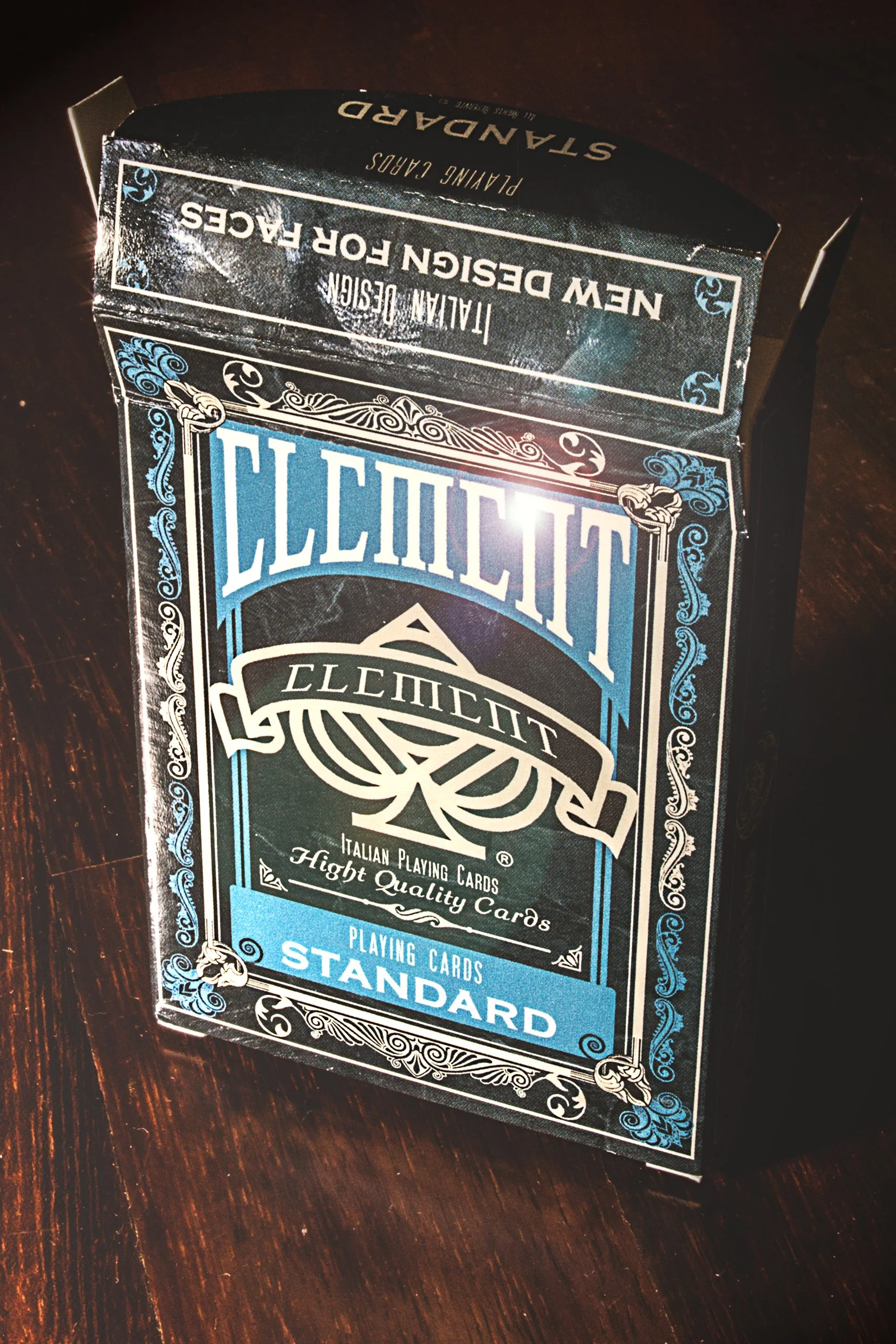 Close-up of a deck of Bicycle playing cards in a black and blue box on a dark wooden surface.