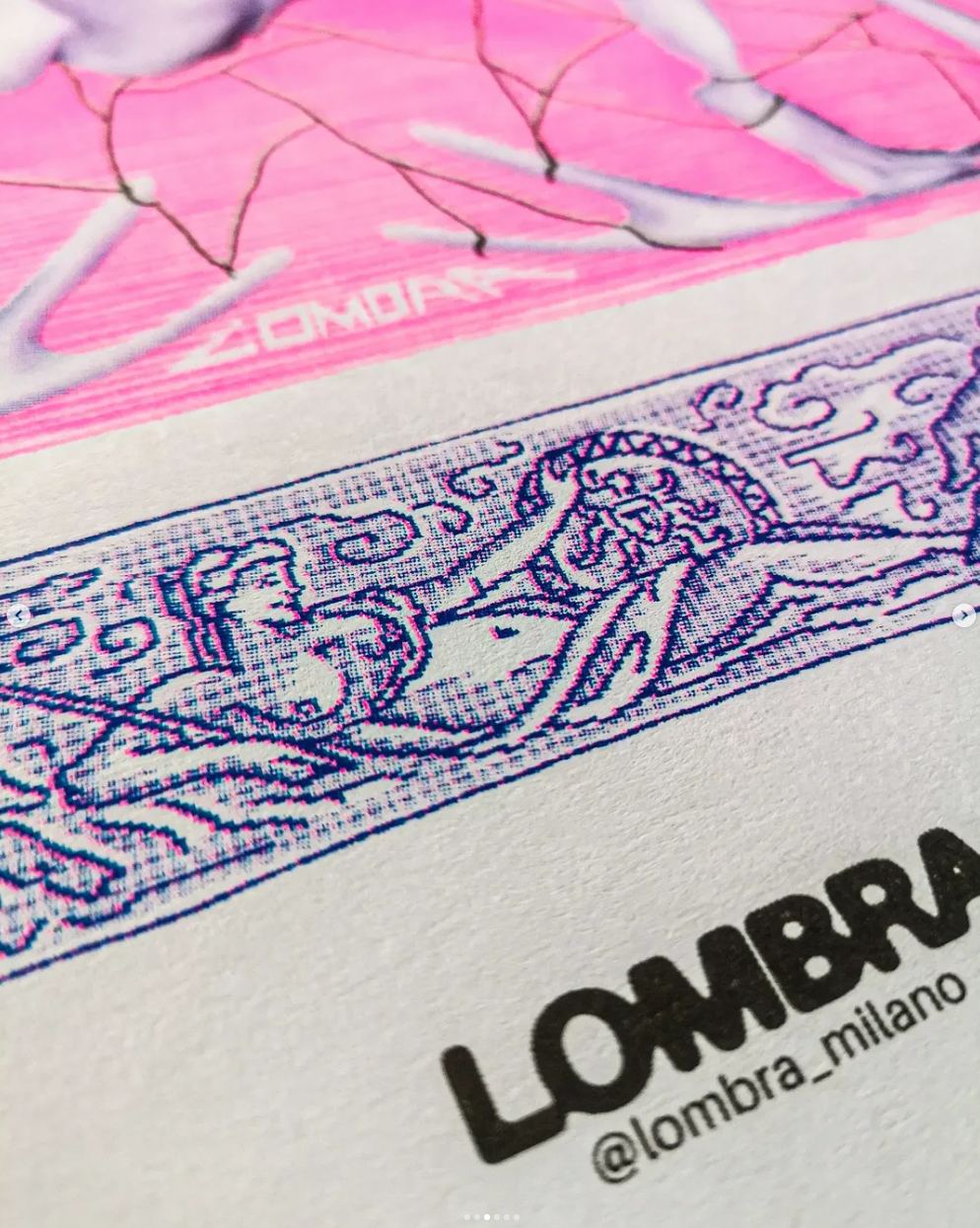Close-up of a printed fabric with a pink background and a detailed line drawing in blue, featuring a figure riding a horse surrounded by decorative elements; text 'LOMBARDA' and Instagram handle '@lombarda_milano' are visible.