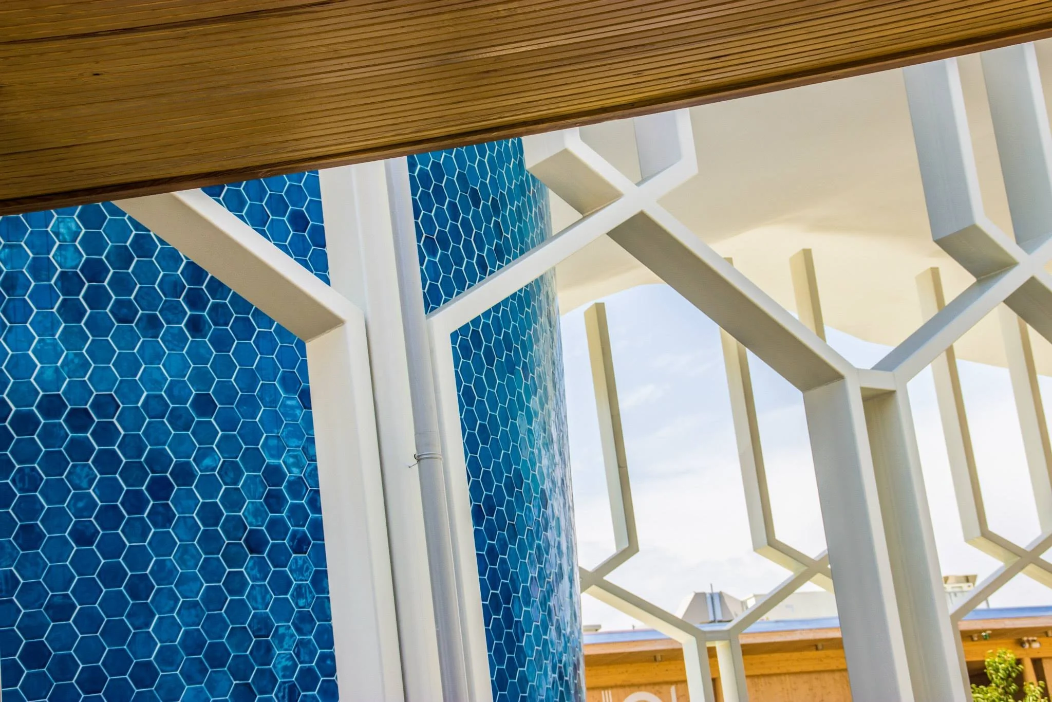 Close-up view of architectural elements featuring blue hexagonal tiles, white structural beams, and a wooden roof.