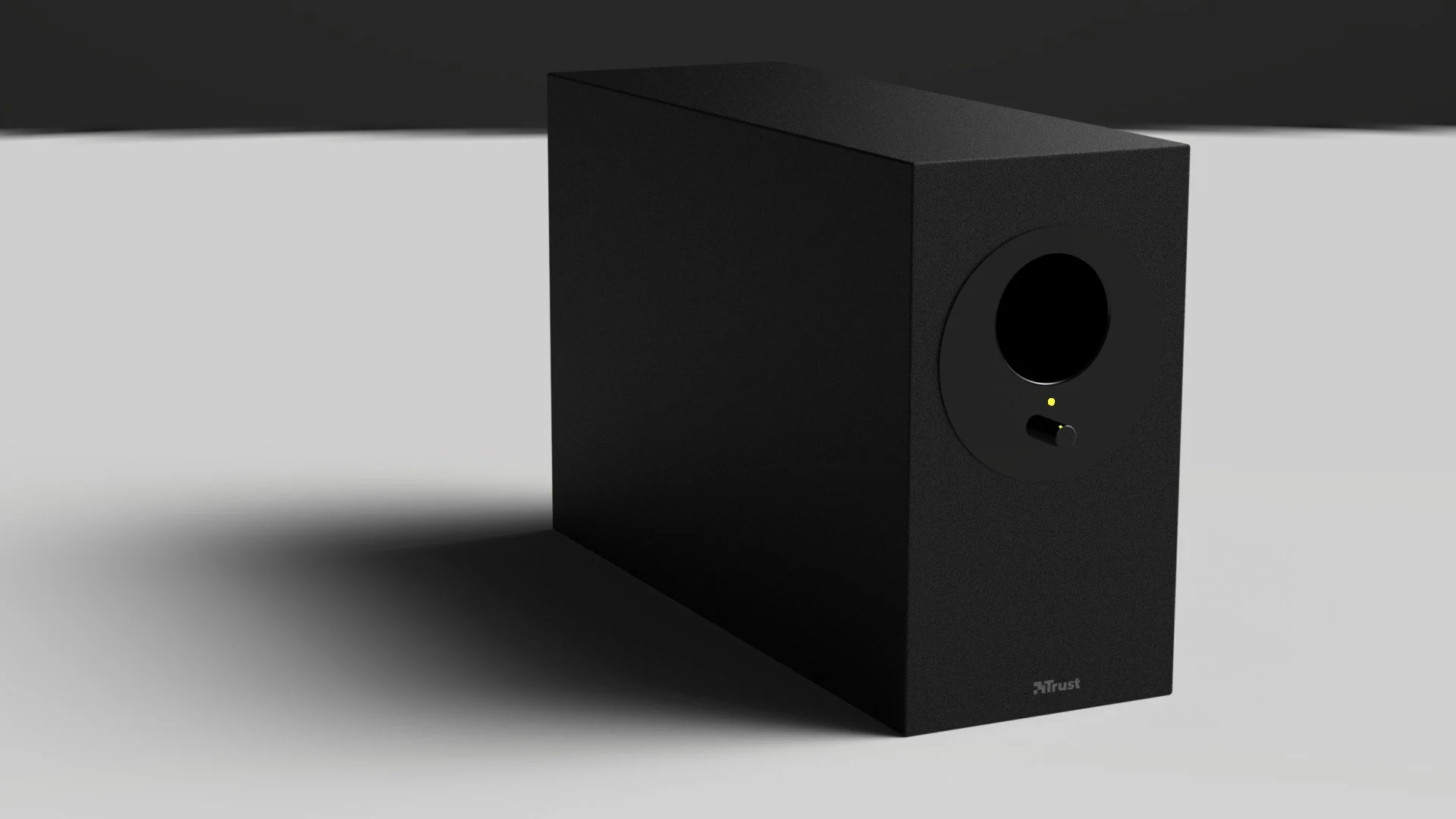 A black Trust brand speaker with a circular speaker grille, a control knob, and indicator lights, placed on a surface with a shadow cast to the left.