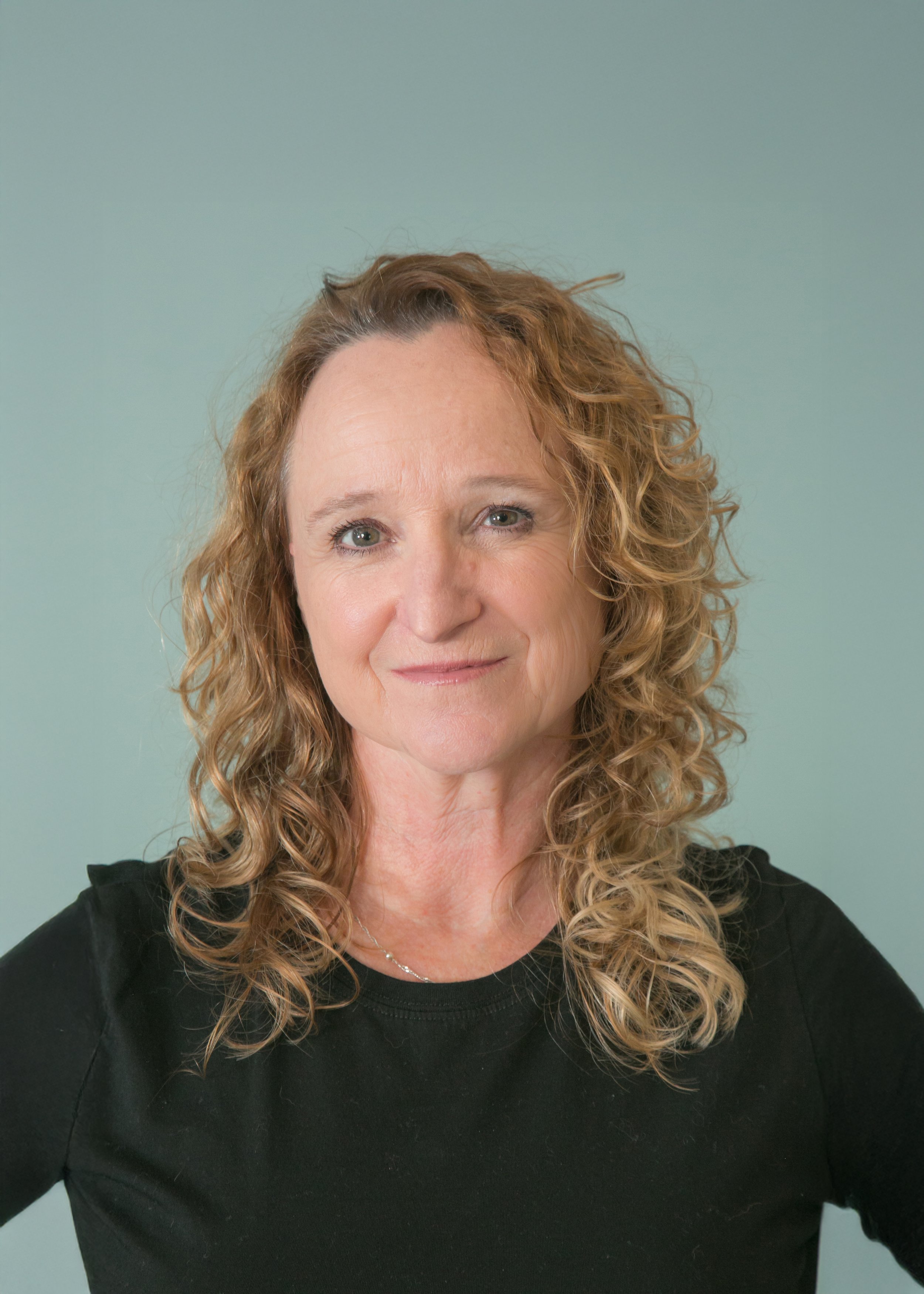 Portrait of a woman with curly blonde hair wearing a black top, against a light green background.