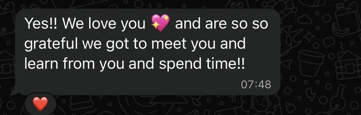 A WhatsApp chat message with white text on a black background. The message says, 'Yes!! We love you 💖 and are so so grateful we got to meet you and learn from you and spend time!!' The message time is 07:48, and there is a red heart emoji below the message.