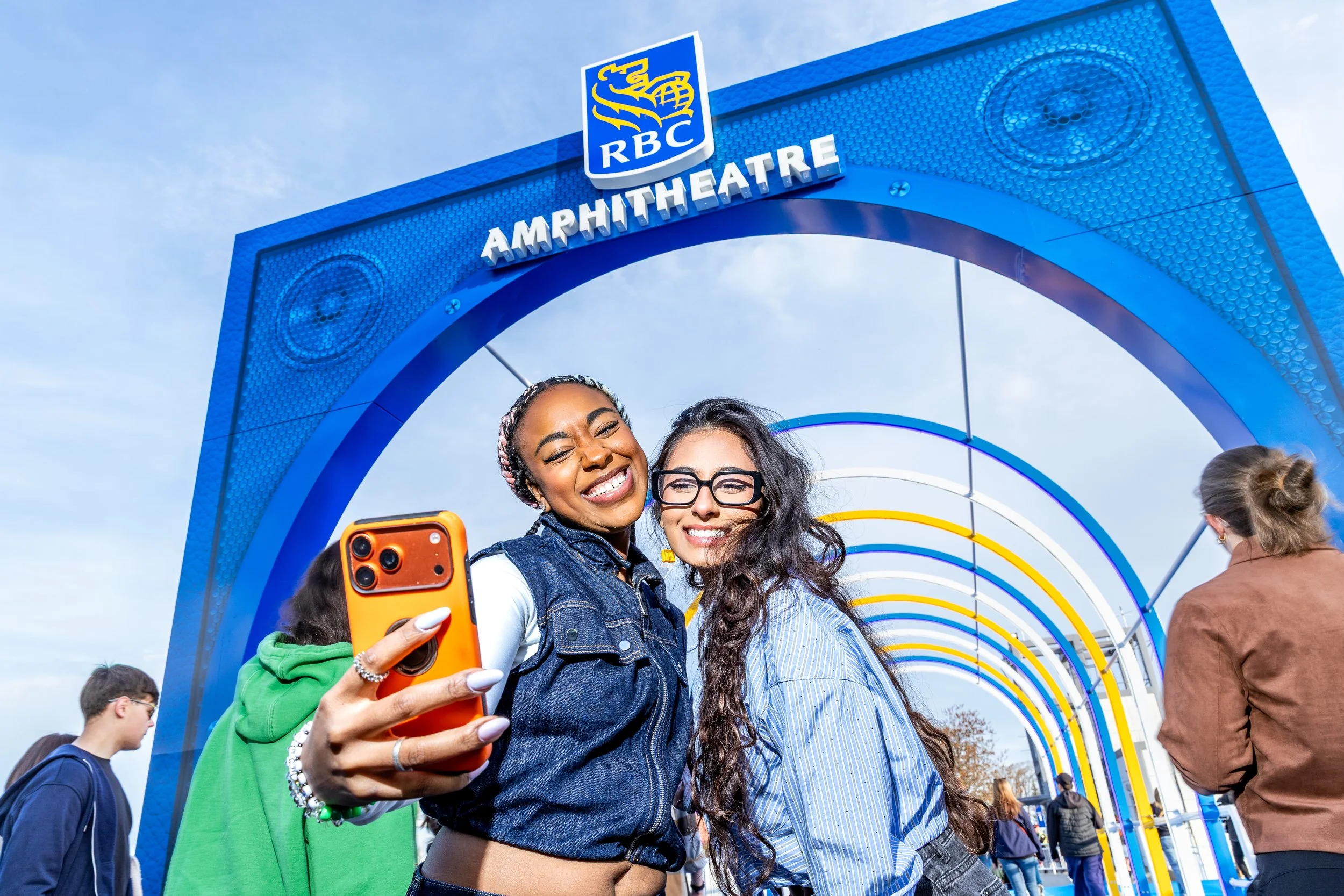 Two women smiling and taking a selfie under a large arch at the RBC Amphitheatre Opening.
