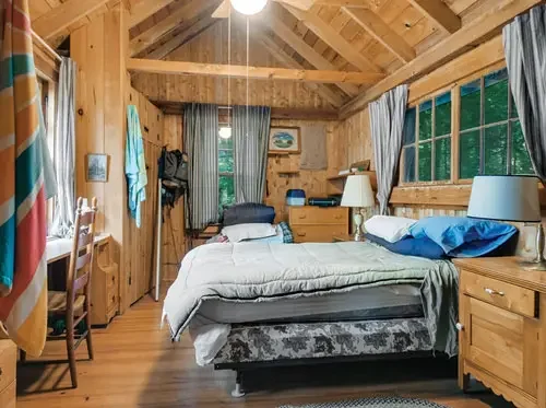 Wood-paneled attic bedroom with a bed, window, and furniture.