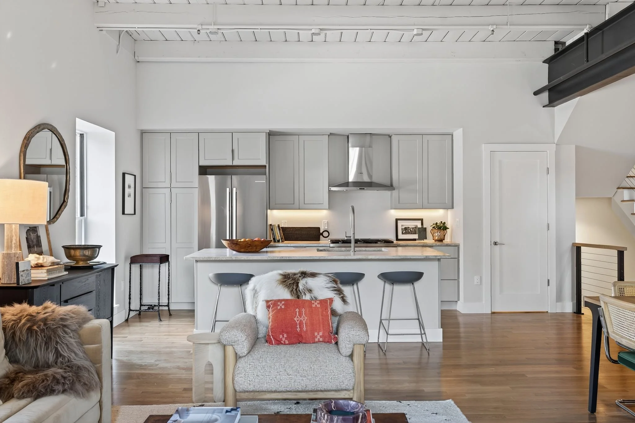 Open-concept kitchen and living room with white cabinets, stainless steel appliances, a kitchen island, and seating area with armchairs and wooden accents.