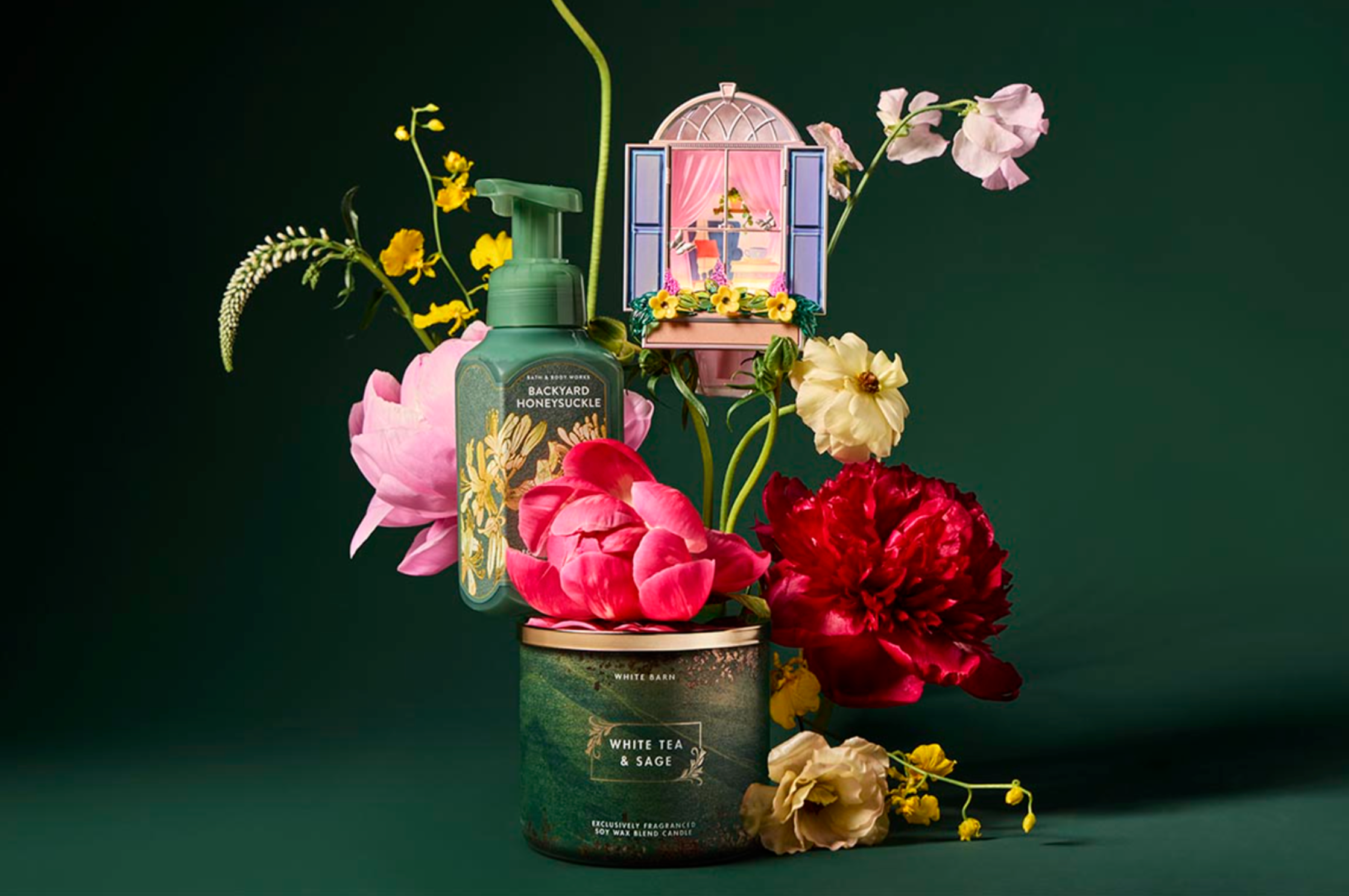A decorative candle labeled 'White Tea & Sage' surrounded by colorful flowers, including pink roses, red peonies, yellow and pink blooms, and a small illustration of a house with pink curtains in a window.