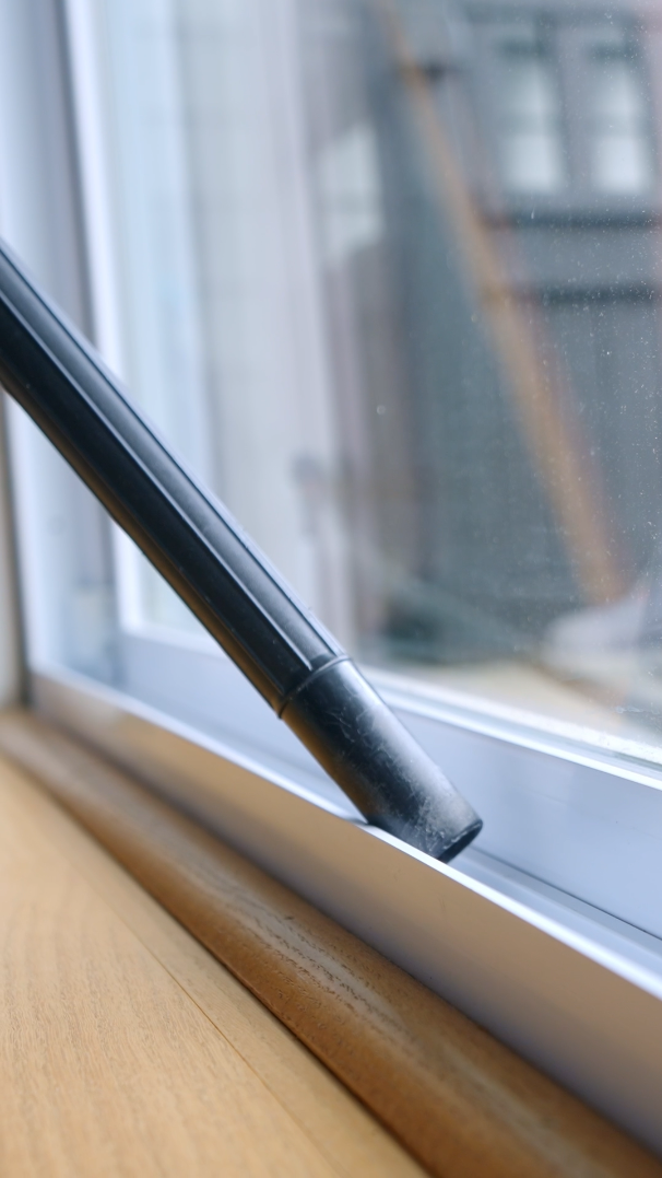 Cleaning a window with a black vacuum or suction tool on a wooden windowsill.
