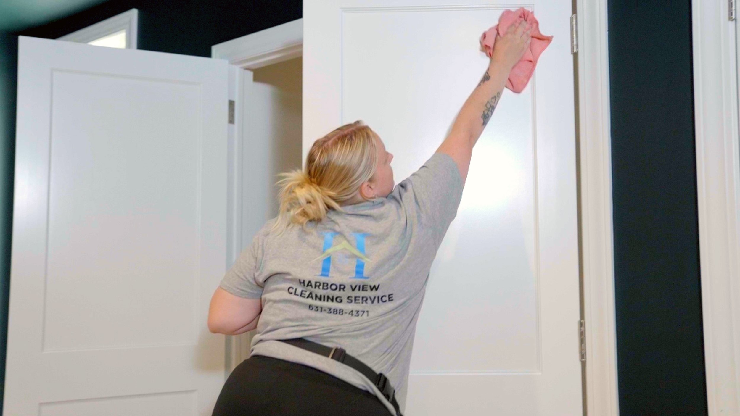 A woman cleaning a white closet door with a pink cloth.