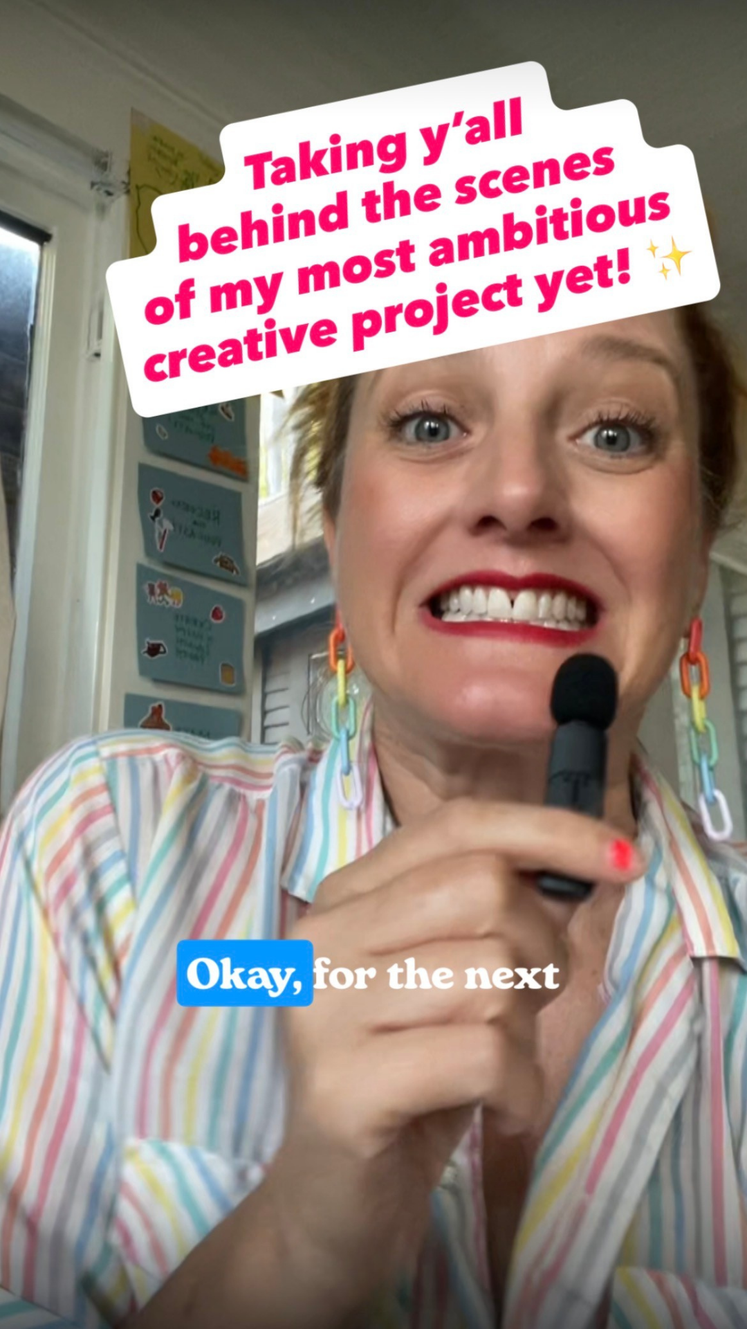 A woman with colorful earrings and a striped shirt holding a microphone, smiling widely with teeth visible, in a room with posters on the wall, with a text overlay saying she is behind the scenes of her creative project.