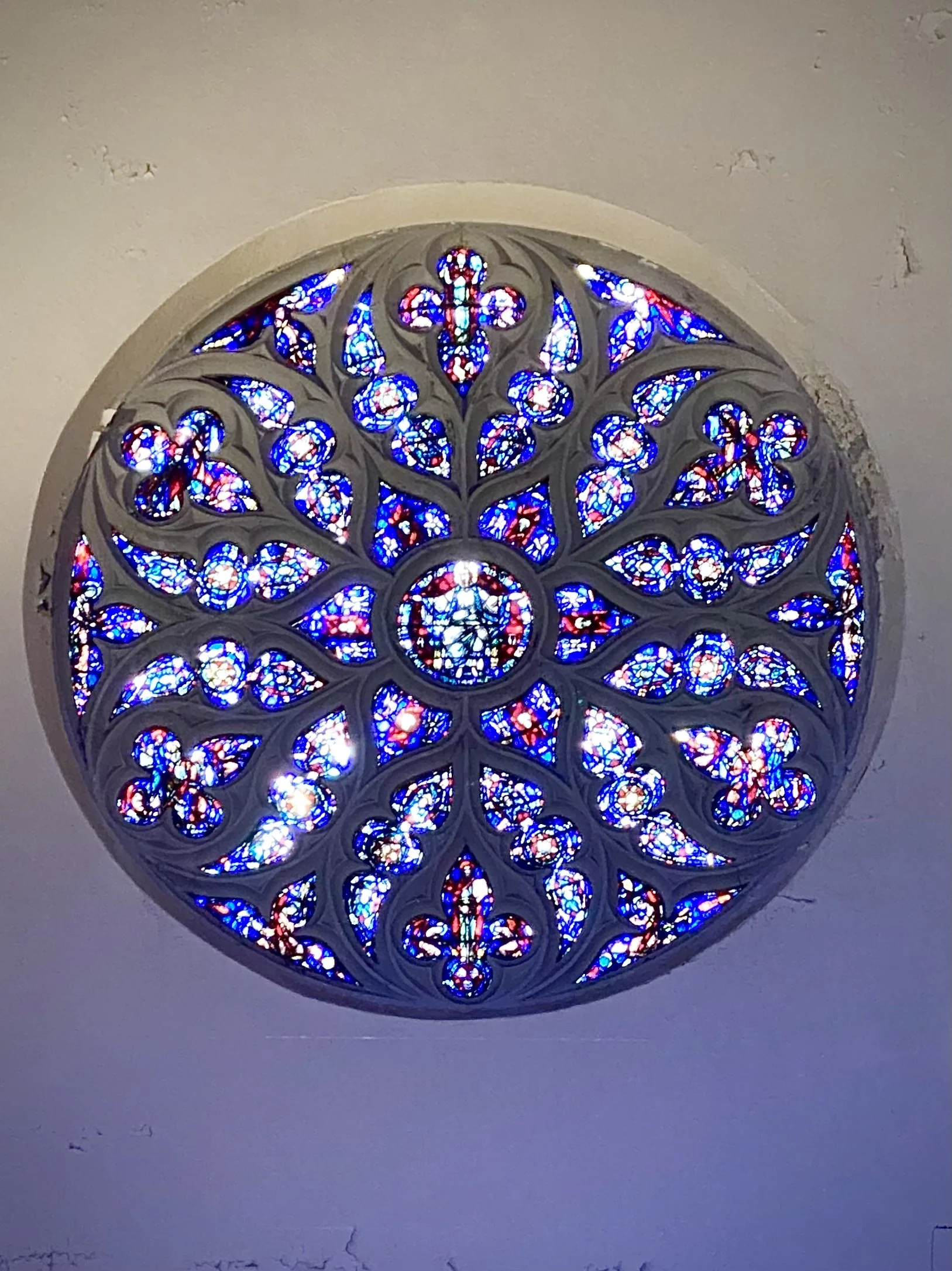 A stained glass window with a circular shape, featuring intricate blue, red, and white patterns, mounted on a white wall.