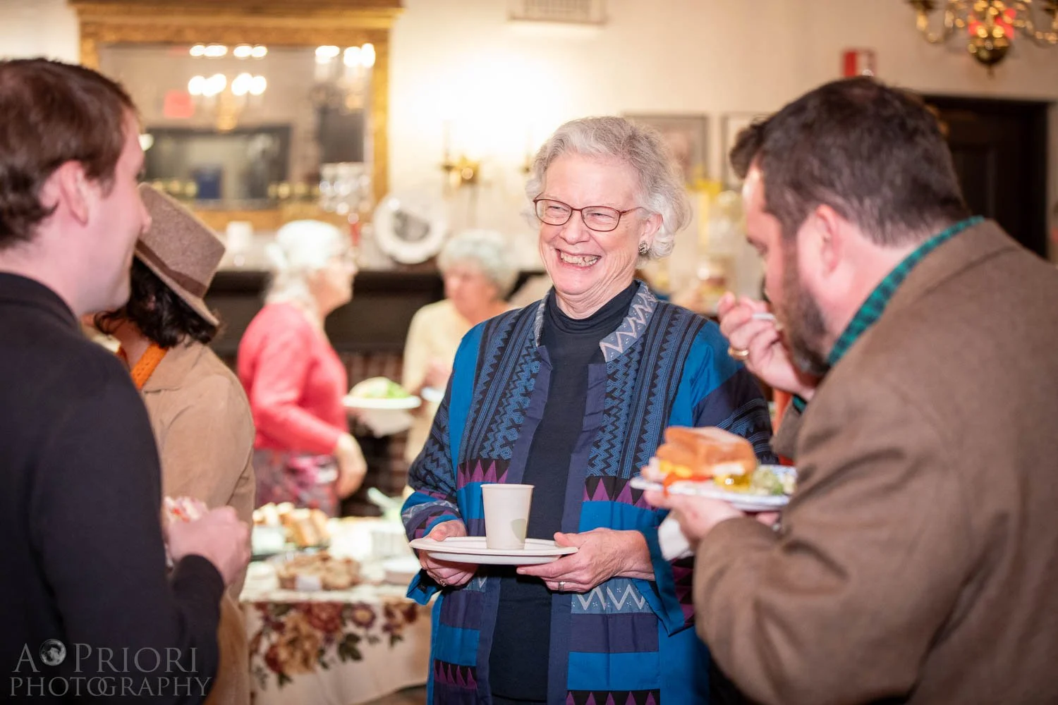 A group of people talking and smiling at a holiday gathering, with a Christmas wreath hanging on the wall in the background.