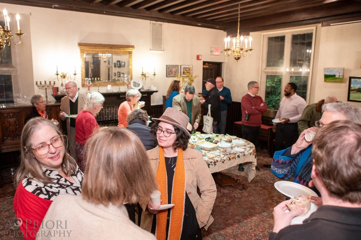 People socializing at a gathering in a warmly lit room with a dining table and traditional decor.