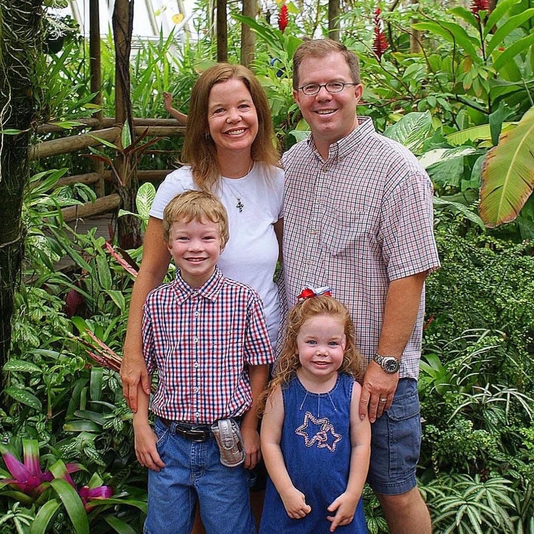 The Sullivan family in a botanical garden on the Fourth of July, parents and two children smiling together outdoors.