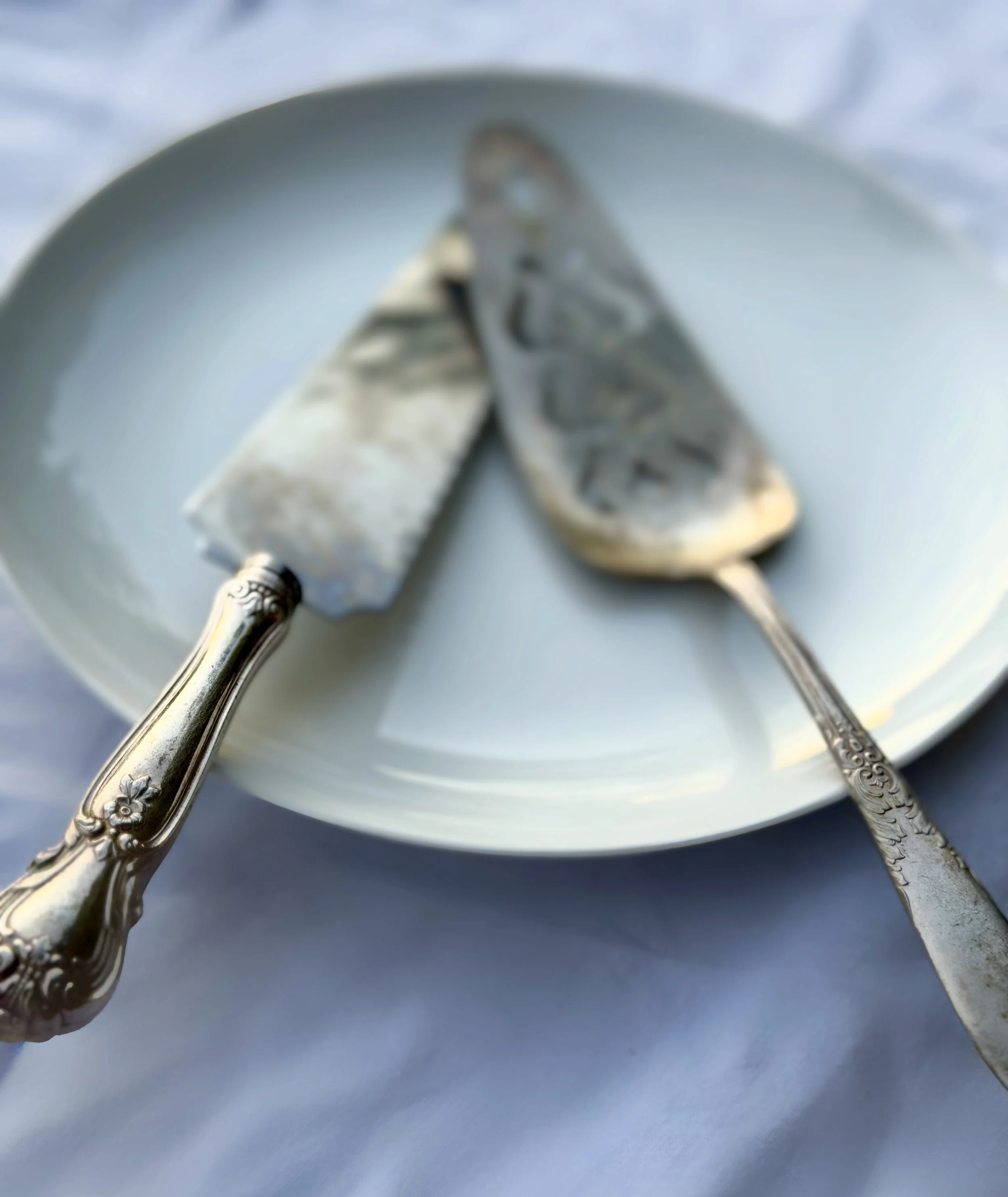 Close-up of a silver spoon and fork with ornate handles on a white plate.
