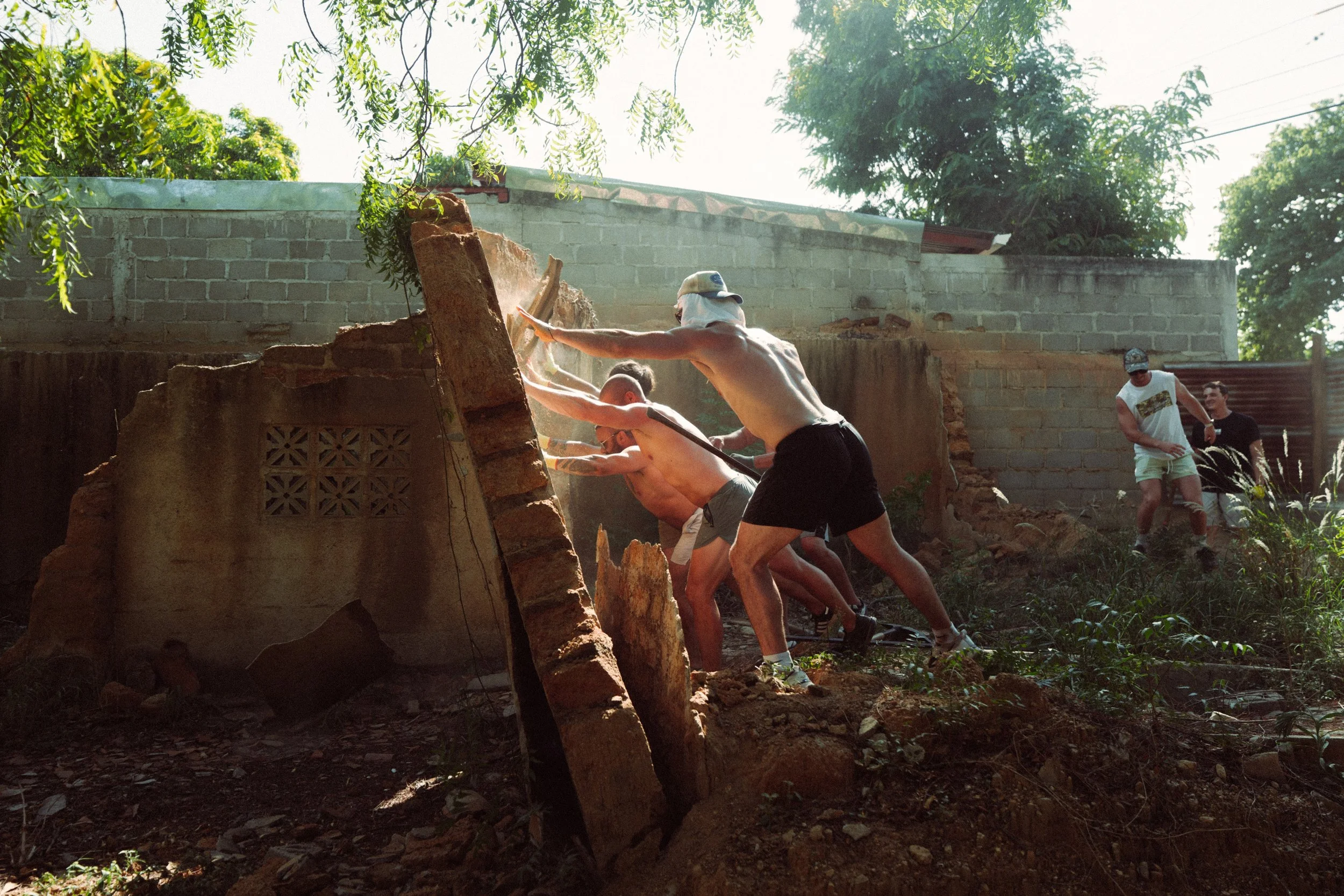 Group of people working together outdoors to move a large tree trunk and debris during a construction or demolition project.