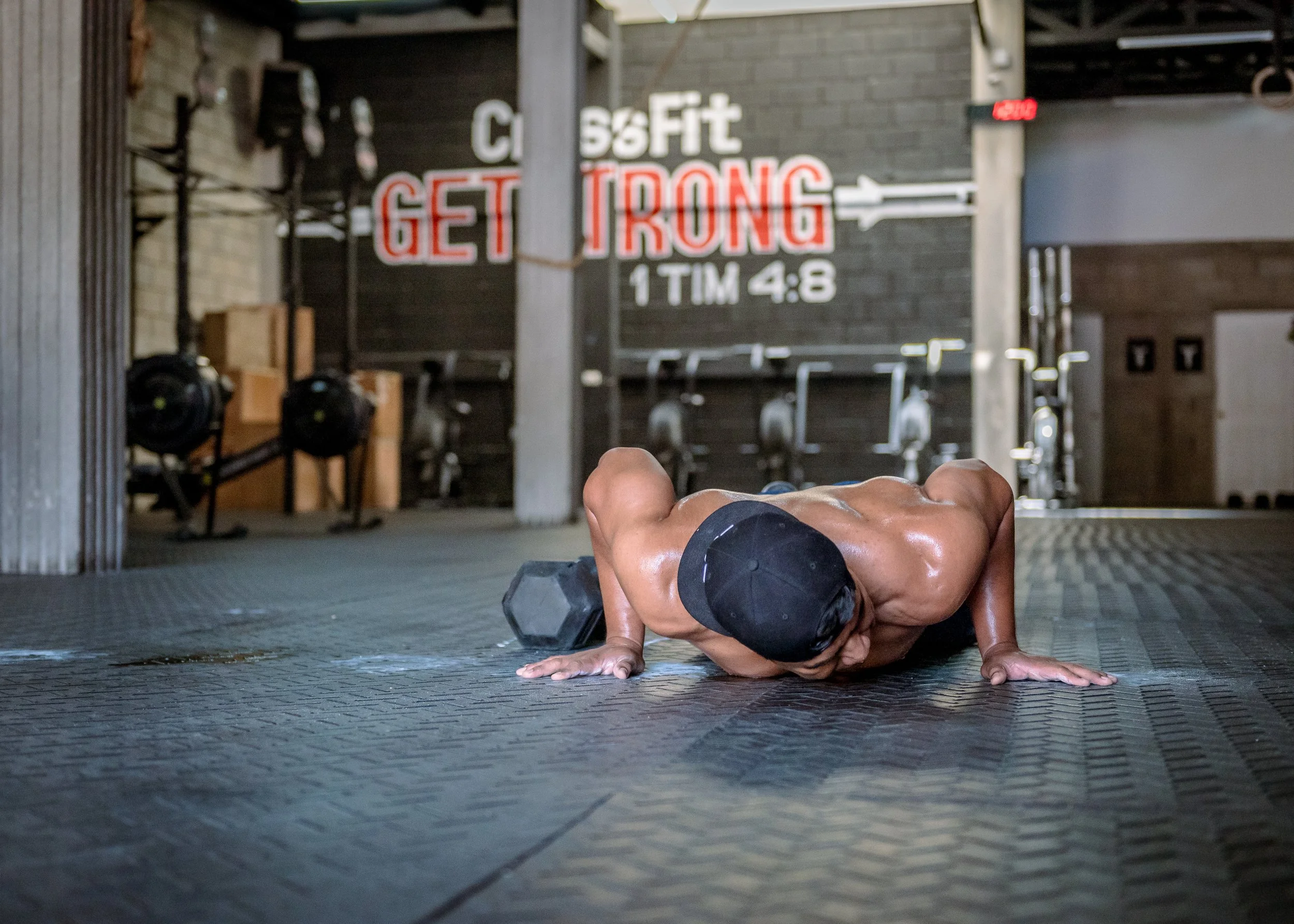 Man performing a push-up with a dumbbell on a gym floor.
