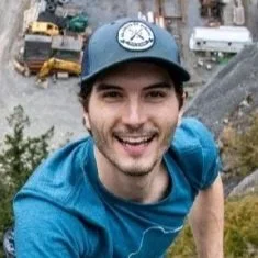 Smiling young man wearing a blue cap and blue shirt outdoors.