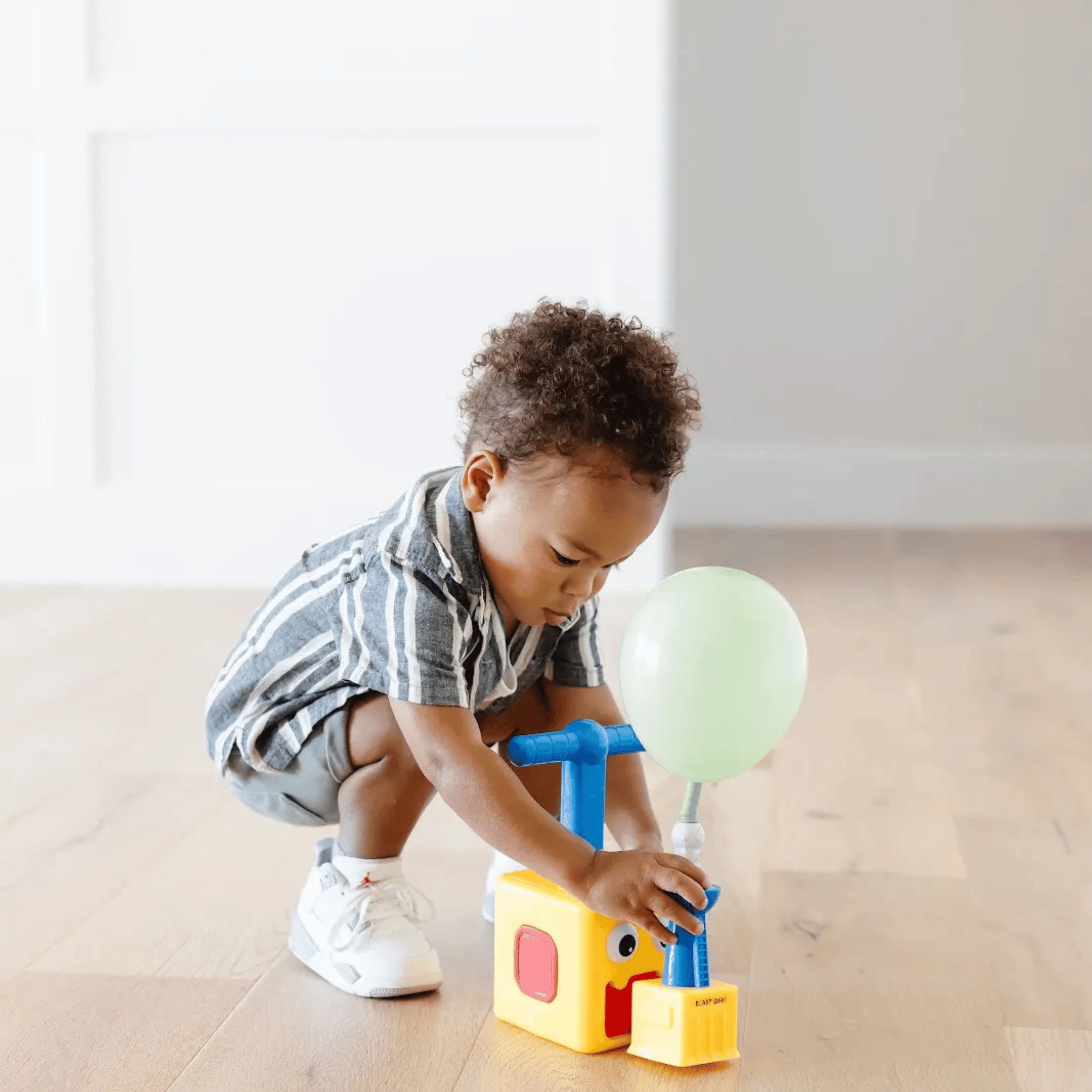 A young child with curly hair playing with colorful toys on a beige floor in a bright room.