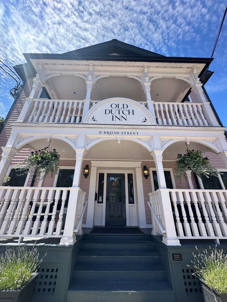 The exterior of the Old Dutch Inn, a pale pink and white wooden house with two stories, front porches, and hanging plants