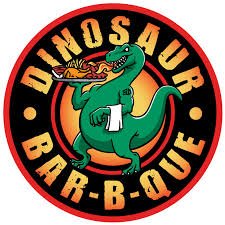 Logo for Dinosaur Bar-B-Que featuring a green dinosaur holding a spatula, with a red and black circular background and text