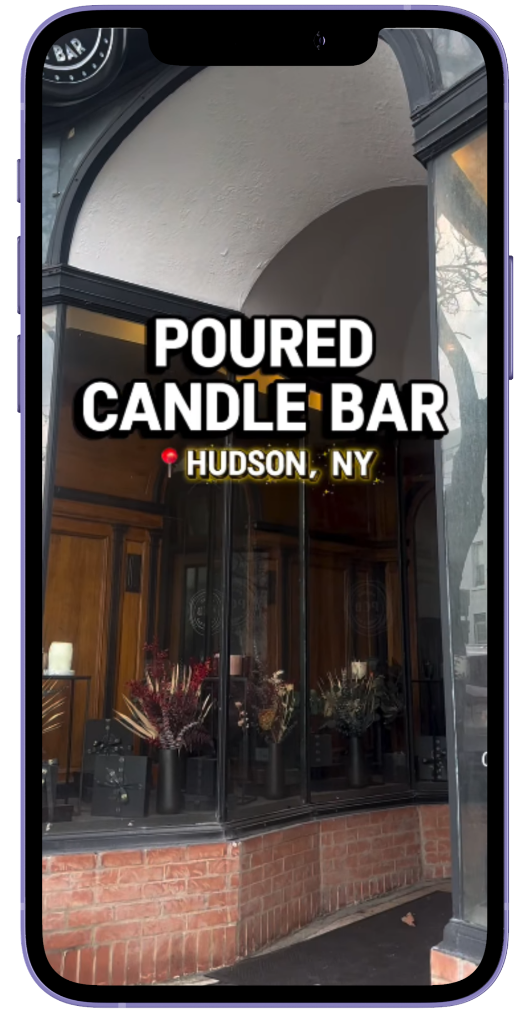 Phone mockup of an Instagram reel featuring Poured Candle Bar, with a low red brick wall and tall windows in the entryway