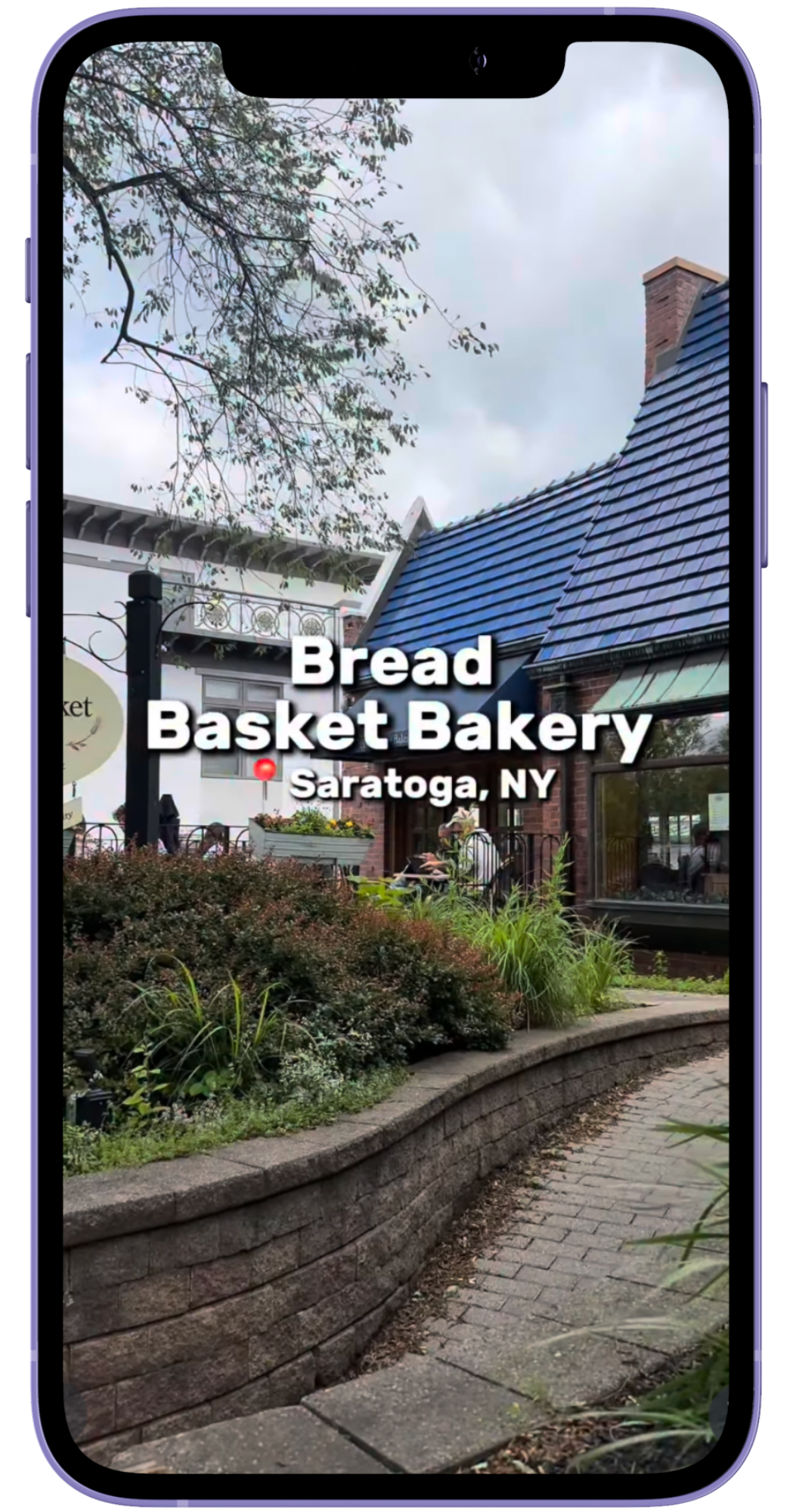 Exterior view of Bread Basket Bakery in Saratoga, NY, with a brick building, blue roof, sidewalk, and landscaped greenery.