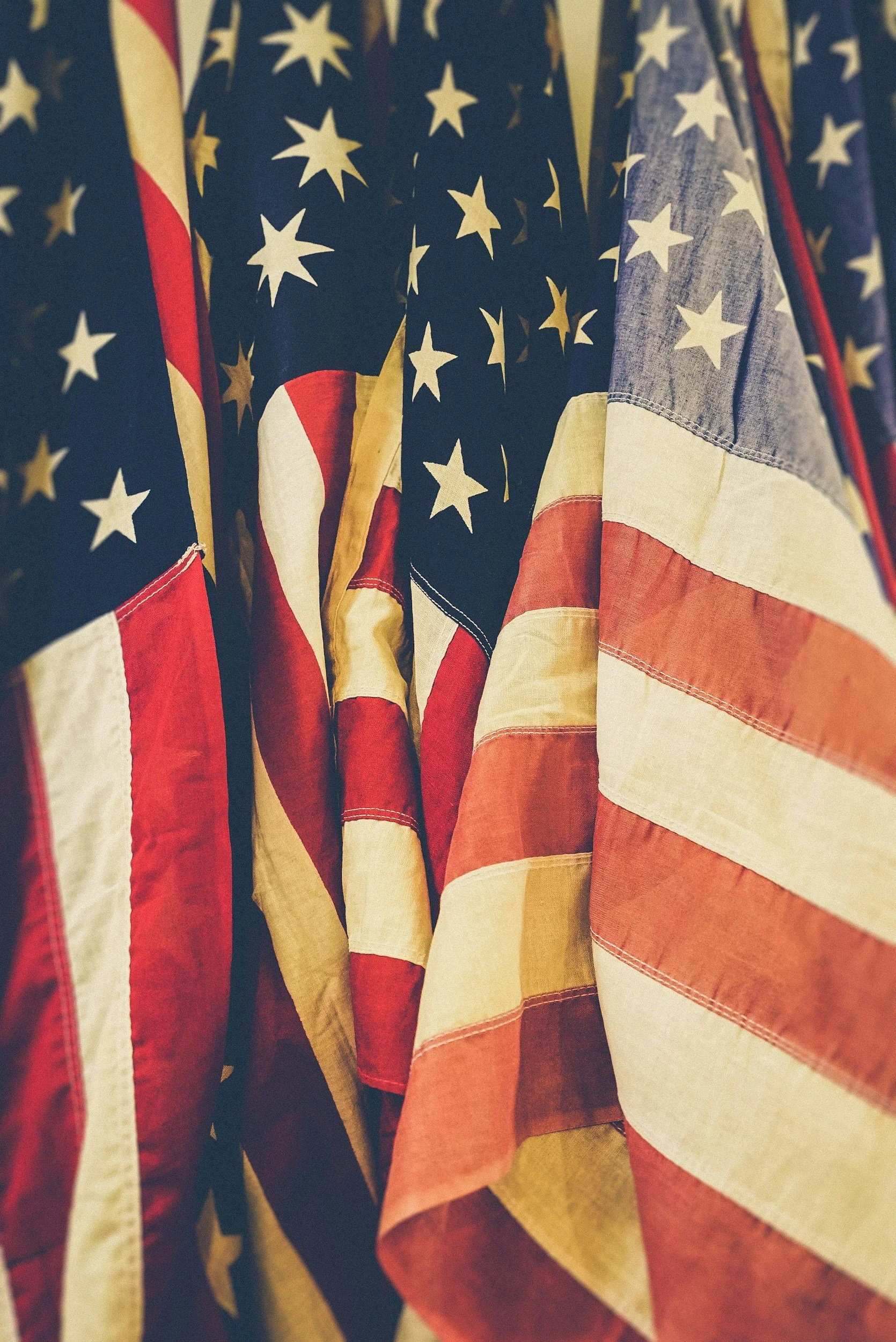 Close-up of multiple American flags hanging together with visible stars and red and white stripes.