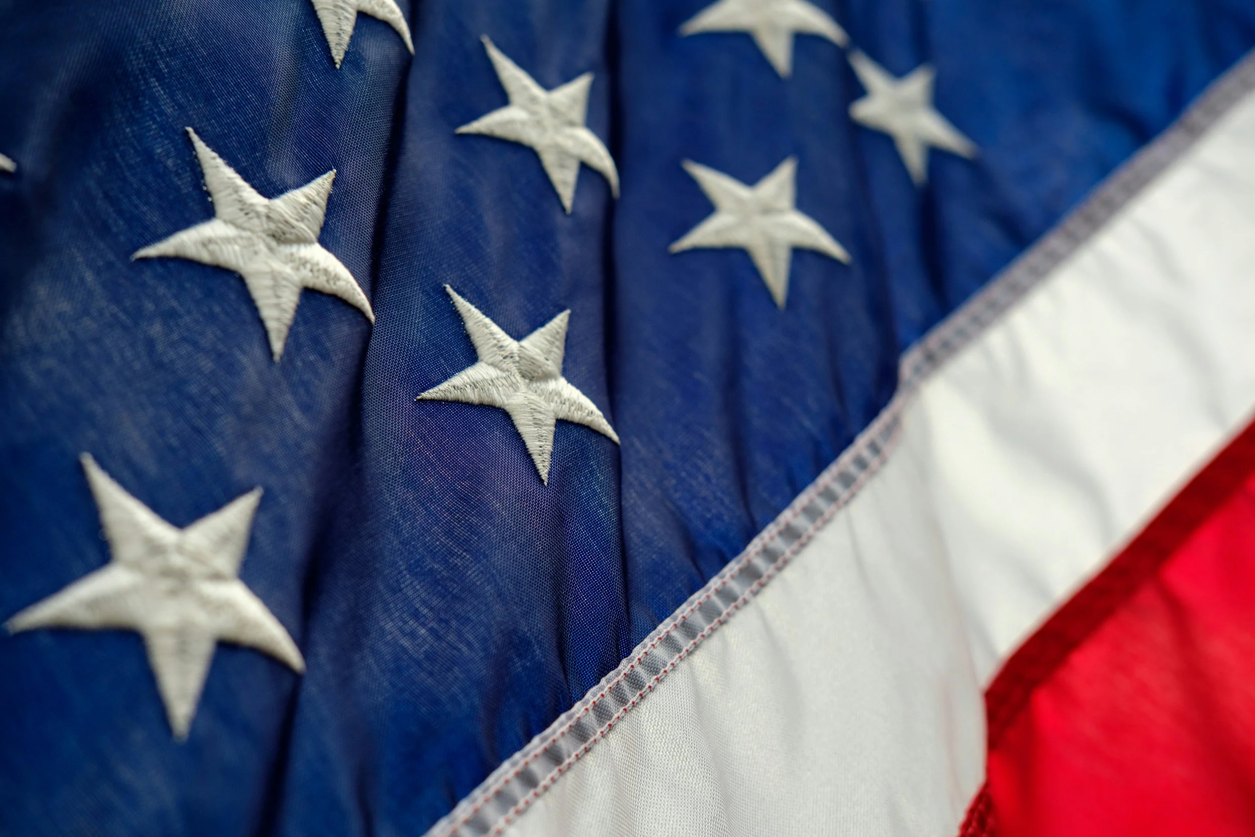 Close-up of an American flag with white embroidered stars on blue fabric and red and white stripes.