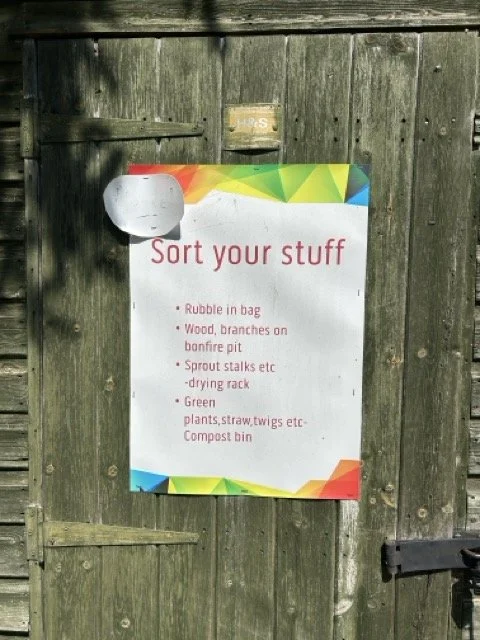 Sign on a wooden fence with instructions to sort trash, listing items like rubble, wood, sprout stalks, green plants, straw, twigs, and compost bin.
