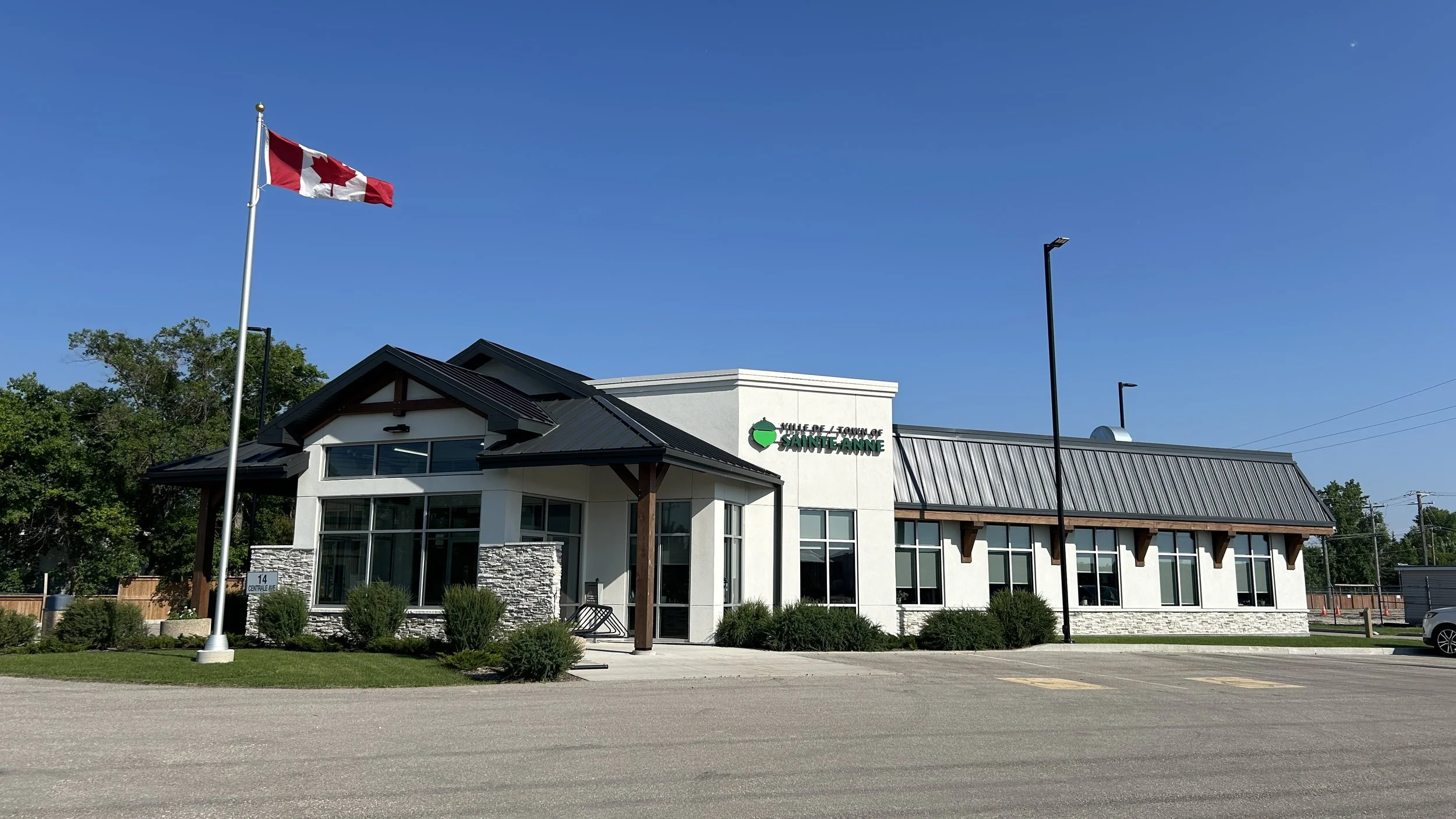 Building with a sign that reads 'Ville de Sainte-Anne', a Canadian flag on a flagpole, and a clear blue sky.