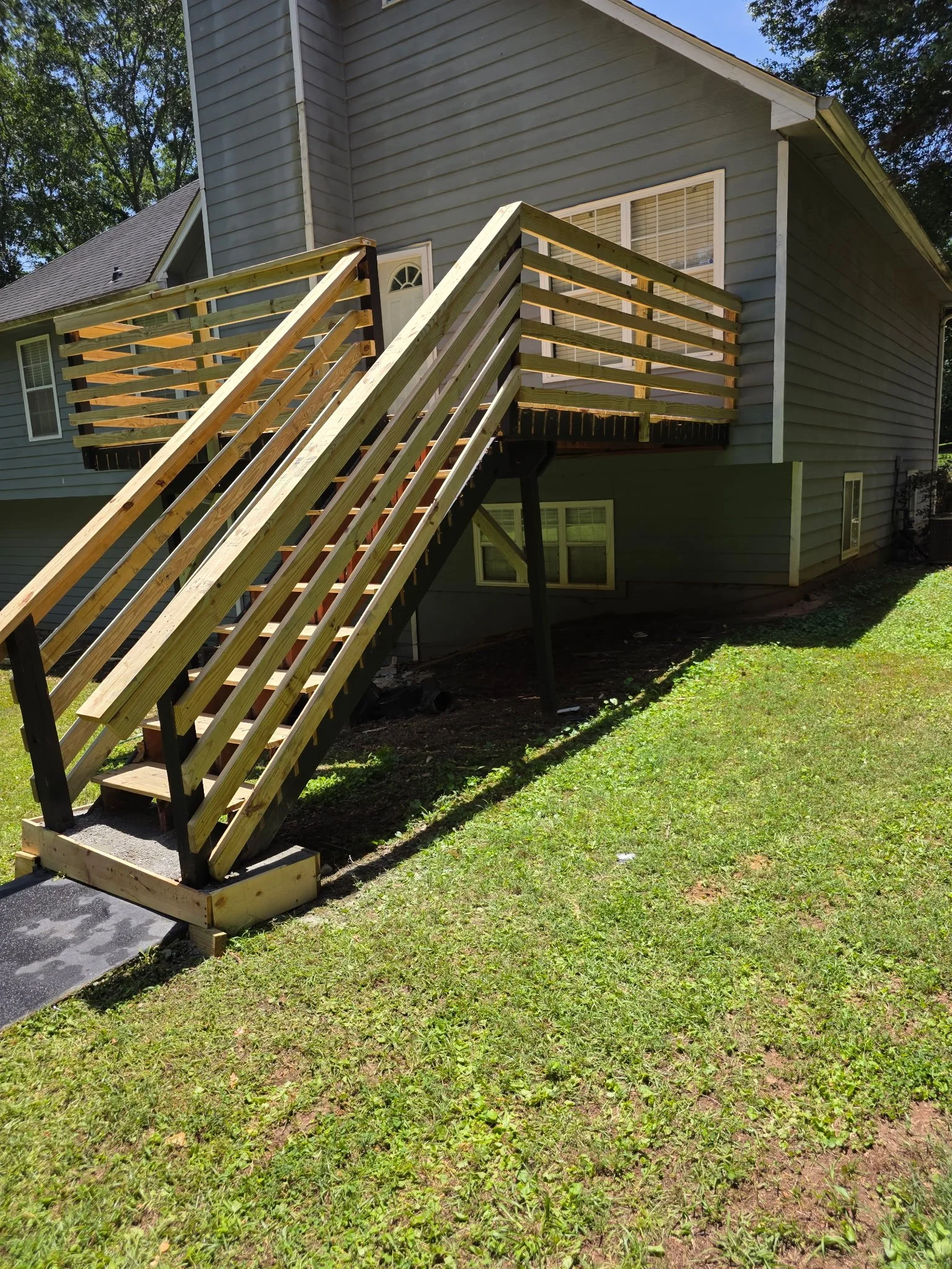 House with new wooden deck and stairs under construction, green grass yard, trees in background.
