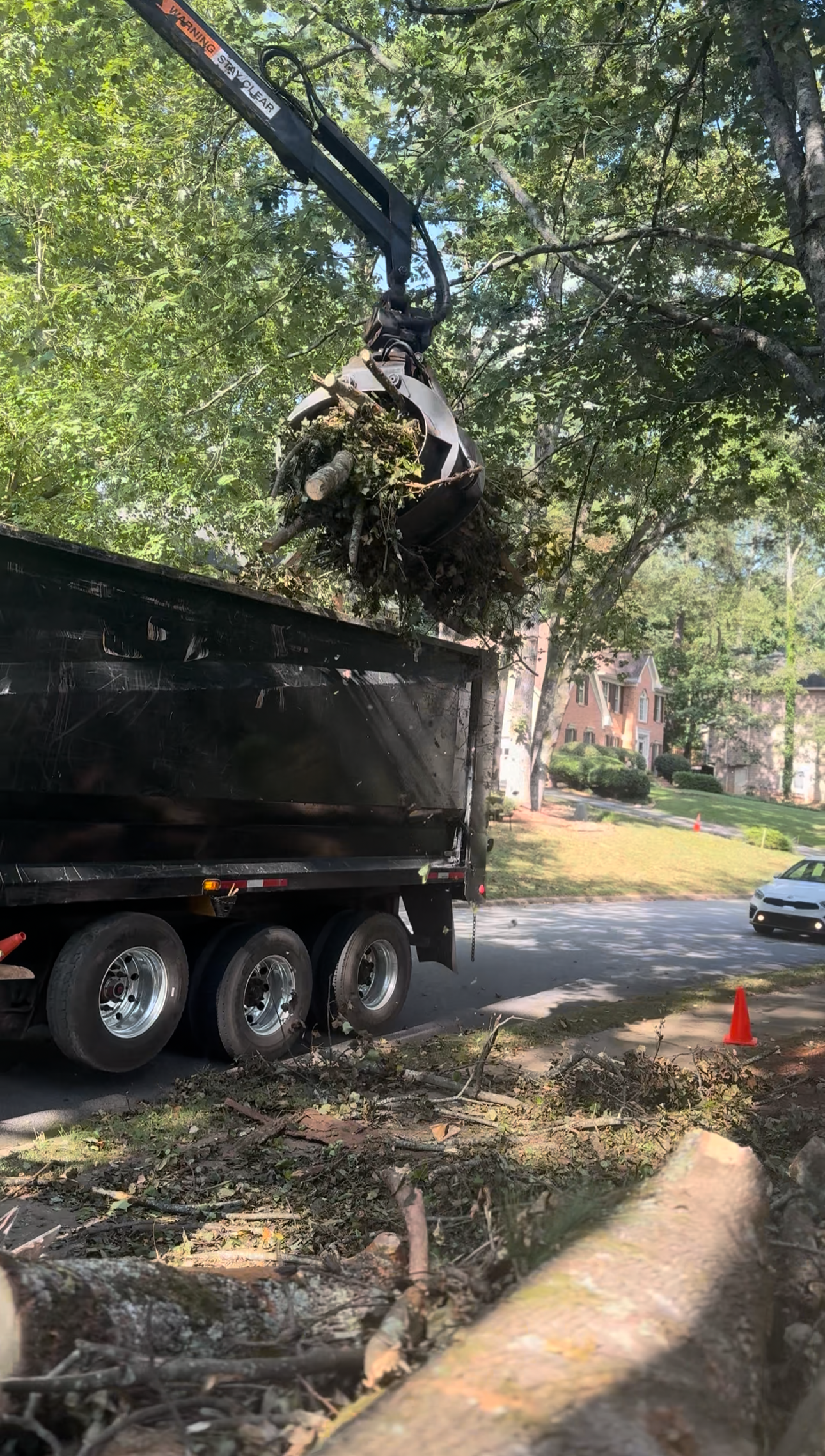 A tree trimming truck lifting a mechanical arm with a grapple attachment to remove tree branches and debris from the street.