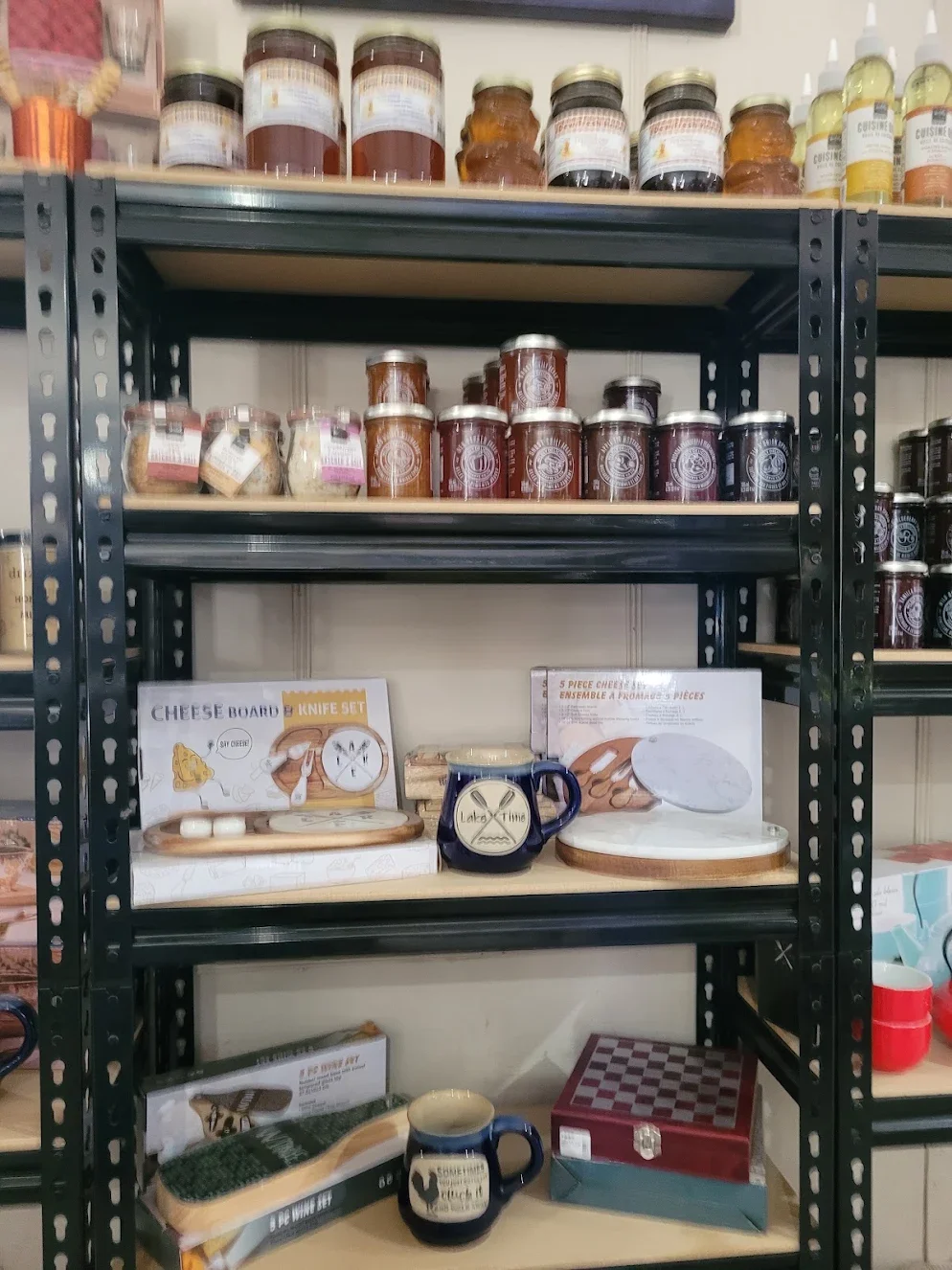 Showcase of various jars of jams and spreads on metal shelving, along with cheese board and tea mugs.