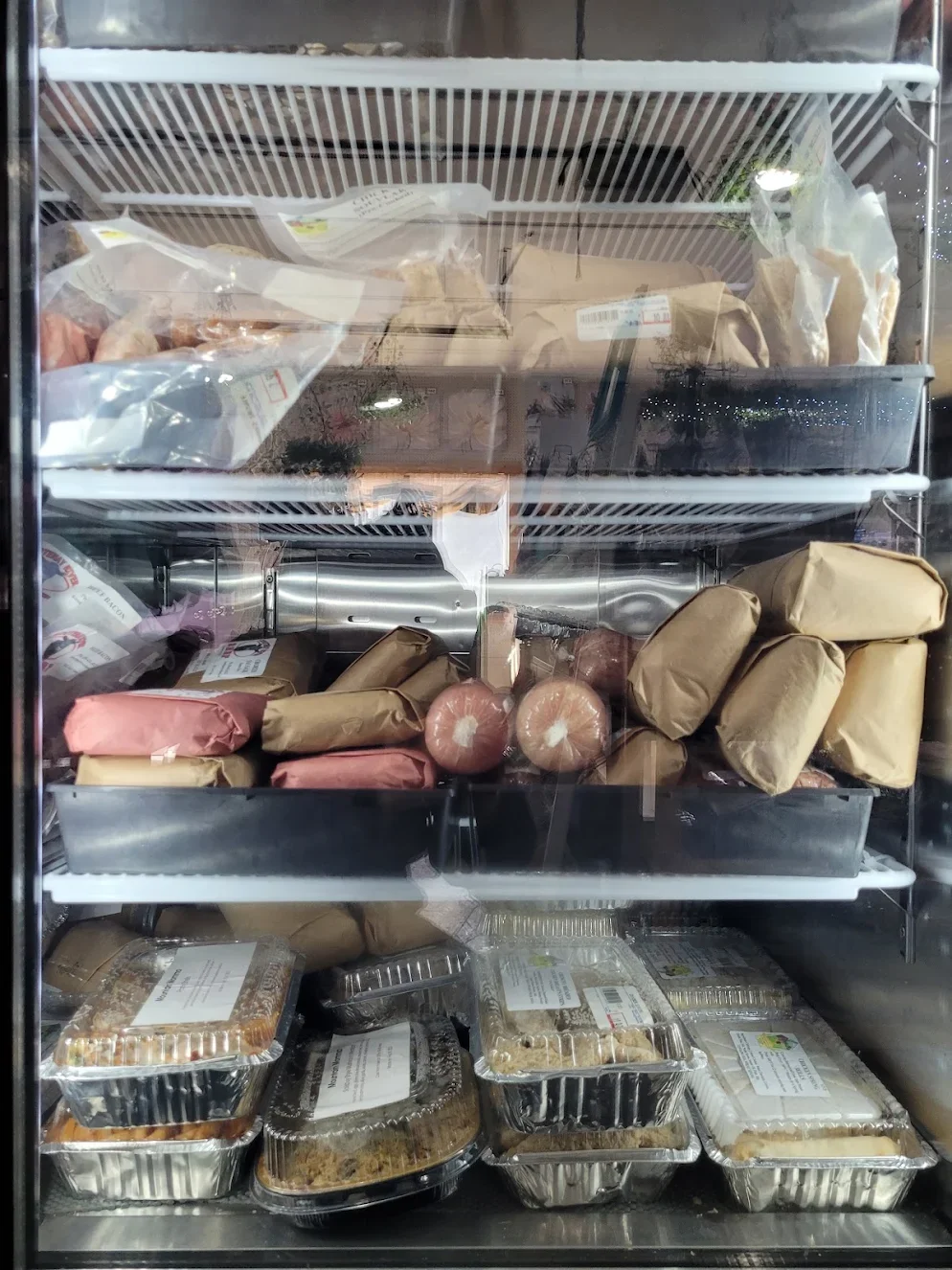 Commercial freezer filled with packaged food items including trays of prepared meals, wrapped sausages, and various frozen products.
