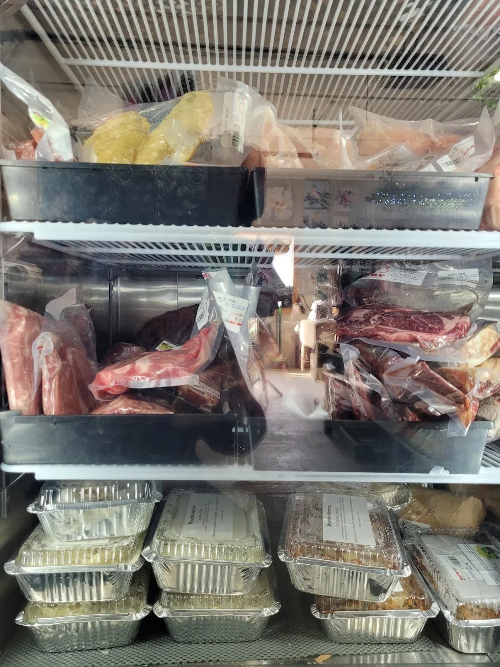 Refrigerator door with various packaged raw meats and prepared food containers inside