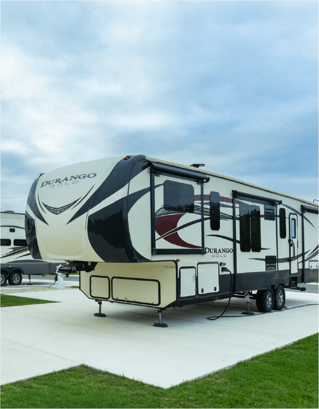 Travel trailer named Durango Gold parked on a concrete pad at Riverfront Village with green grass nearby under a cloudy sky.