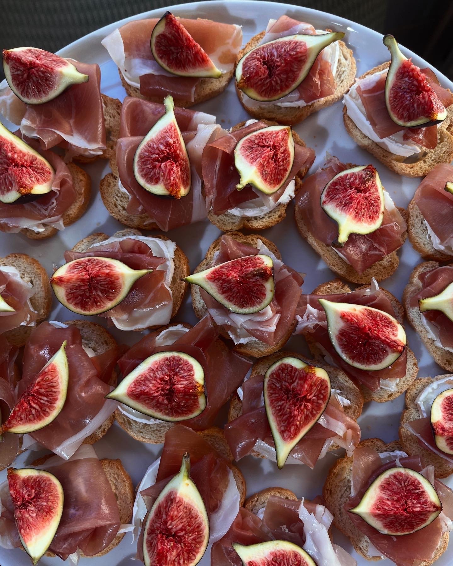 Assorted crostini with figs, prosciutto, cheese, and bread slices arranged on a white tray.