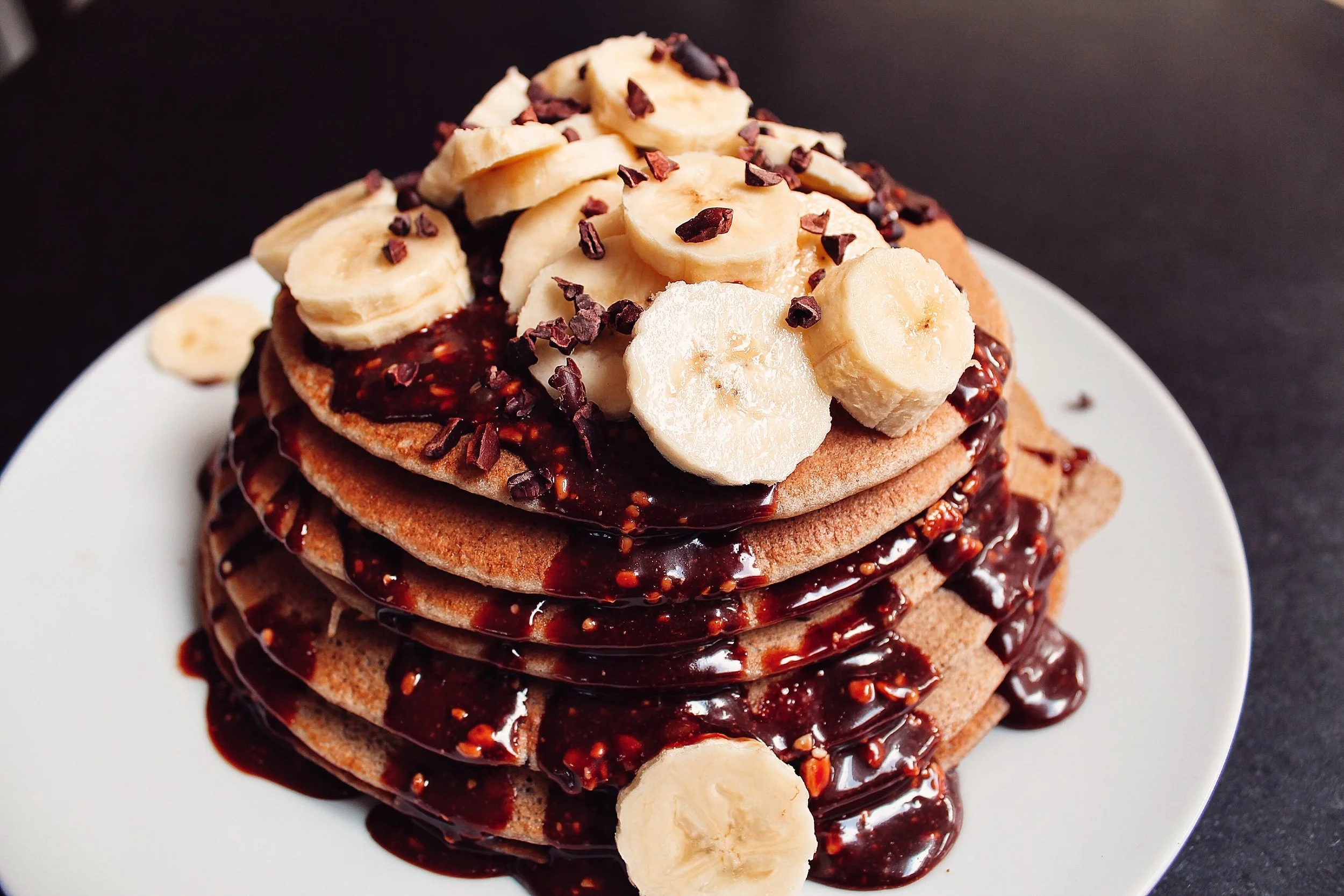 Stacked cookies topped with sliced bananas, chocolate chips, and drizzled with chocolate syrup on a white plate.