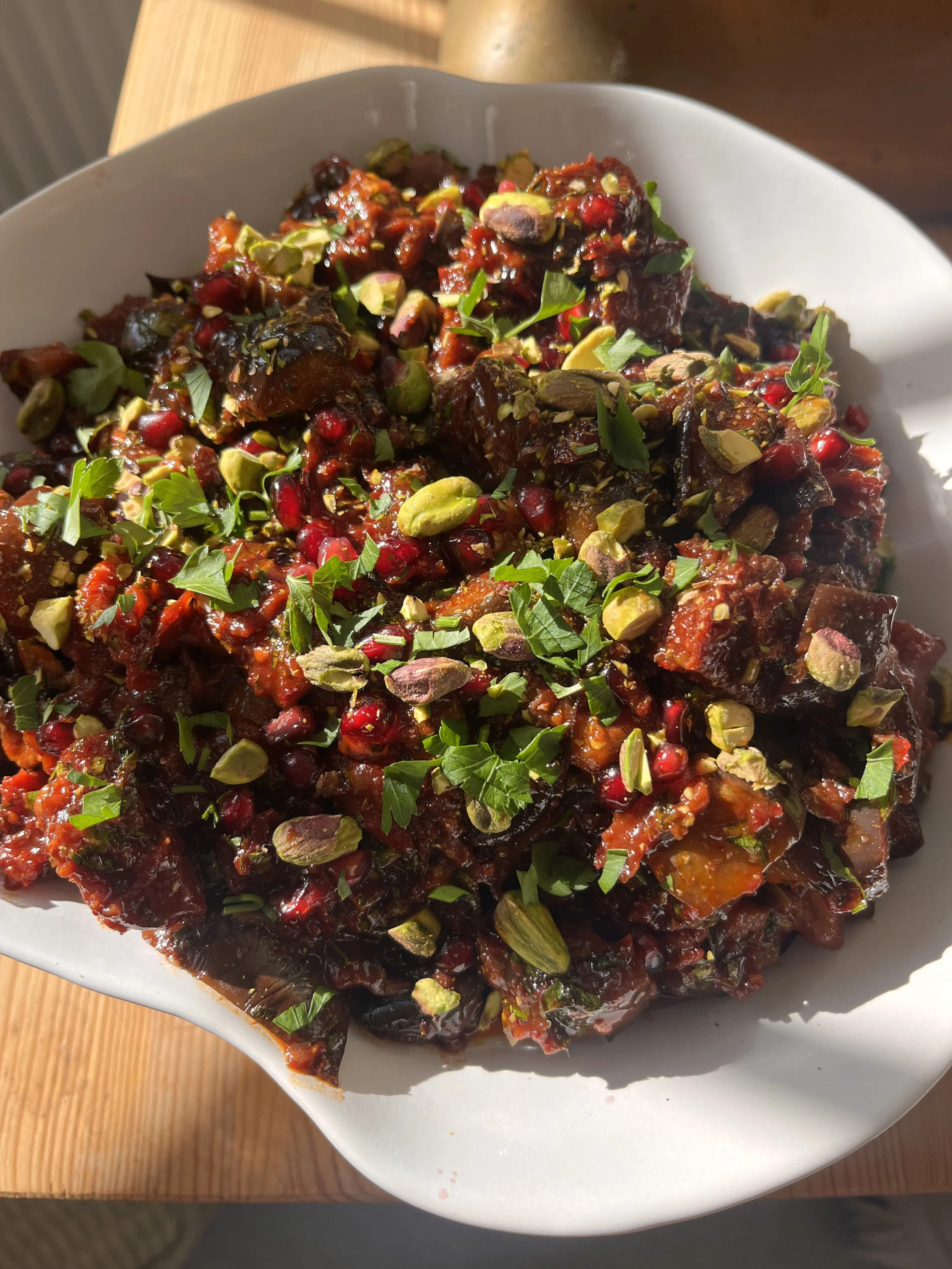 A white bowl filled with a dark red and green salad topped with chopped green herbs, pumpkin seeds, and pomegranate seeds, placed on a wooden surface.