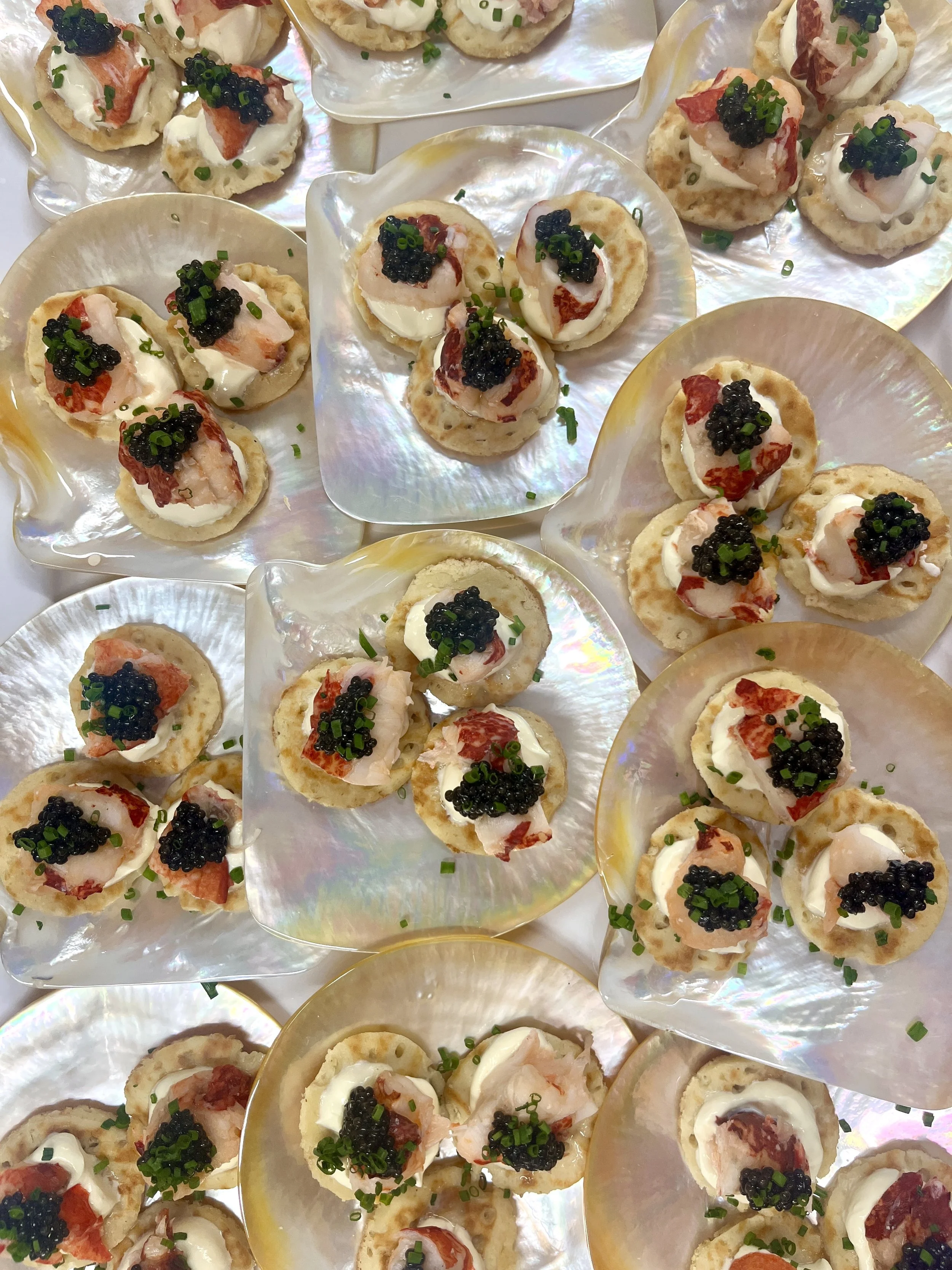 Tiny appetizers on shells with white cream, shrimp, red bacon, black caviar, and chopped green onions garnished with chives.