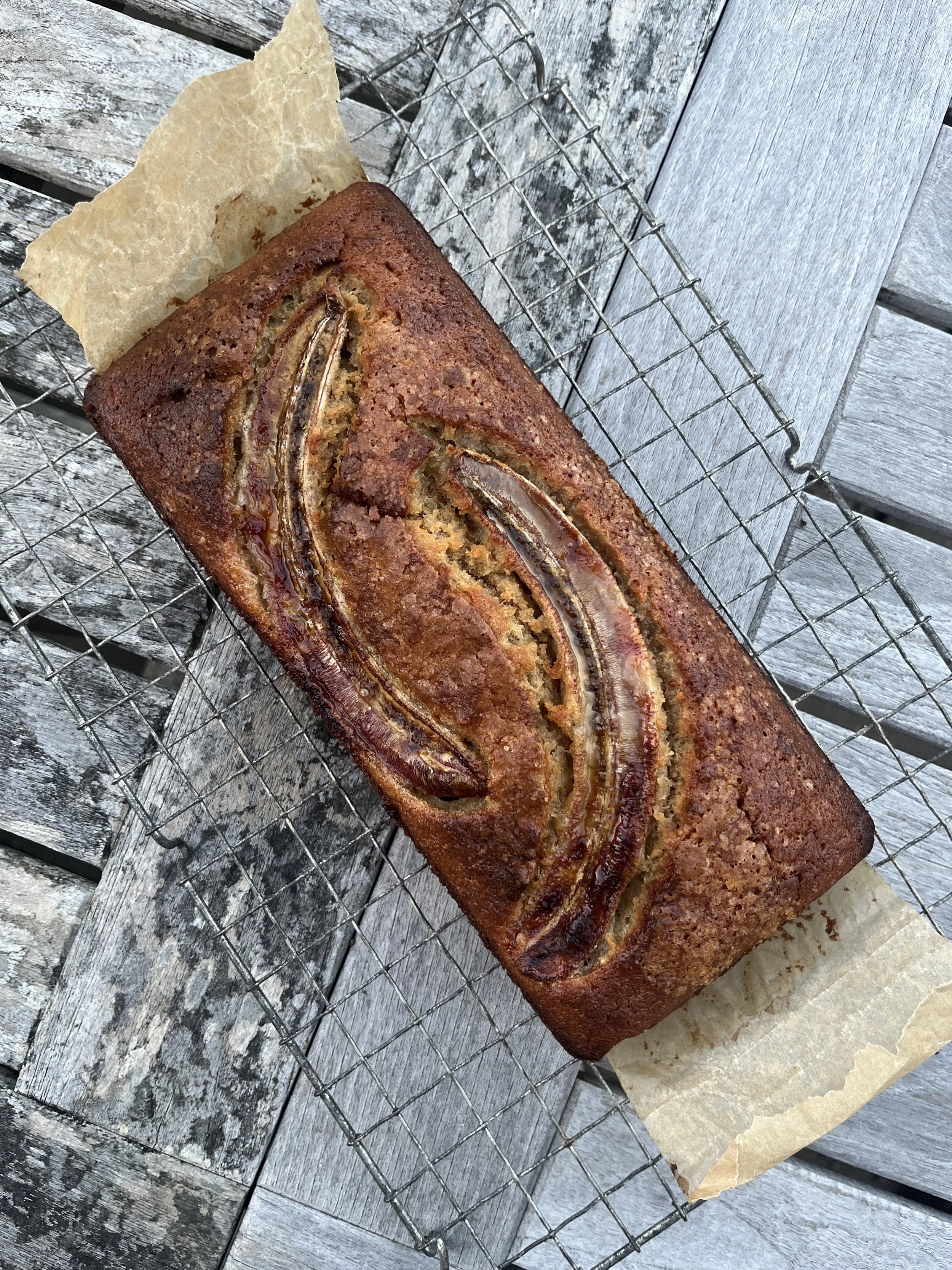 Banana bread on a cooling rack placed on a weathered wooden surface, with a piece of parchment paper underneath.